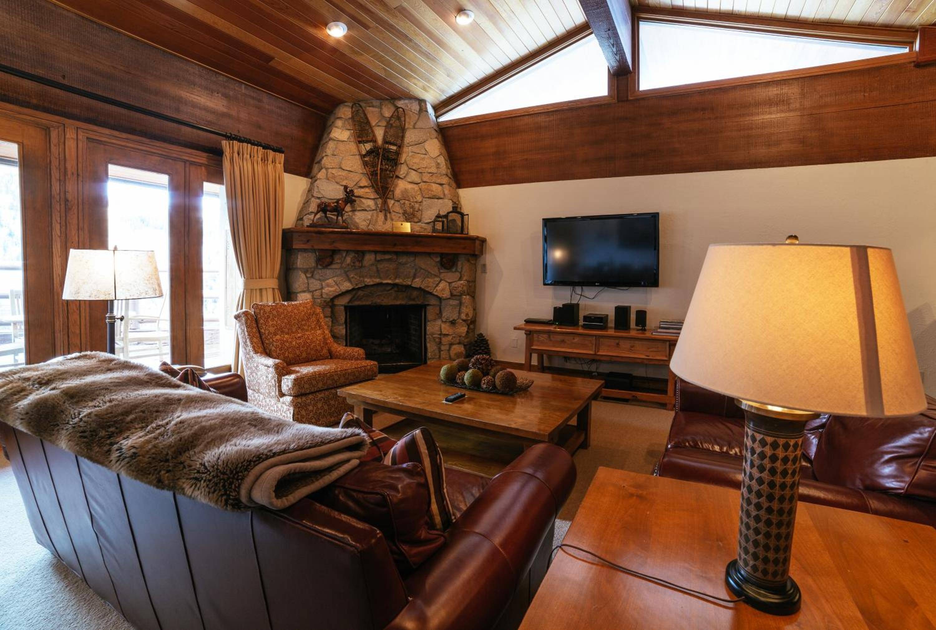 Warm wood paneling and a crackling stone fireplace create an intimate mountain retreat, where leather seating and natural textures invite après-ski relaxation beneath soaring timber beams.