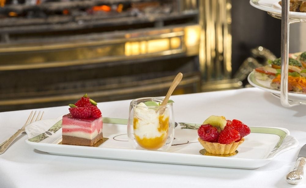 Delicate afternoon tea treats arrive on fine china—layered strawberry cake, passion fruit parfait, and berry tart showcase the kitchen's refined pastry artistry.
