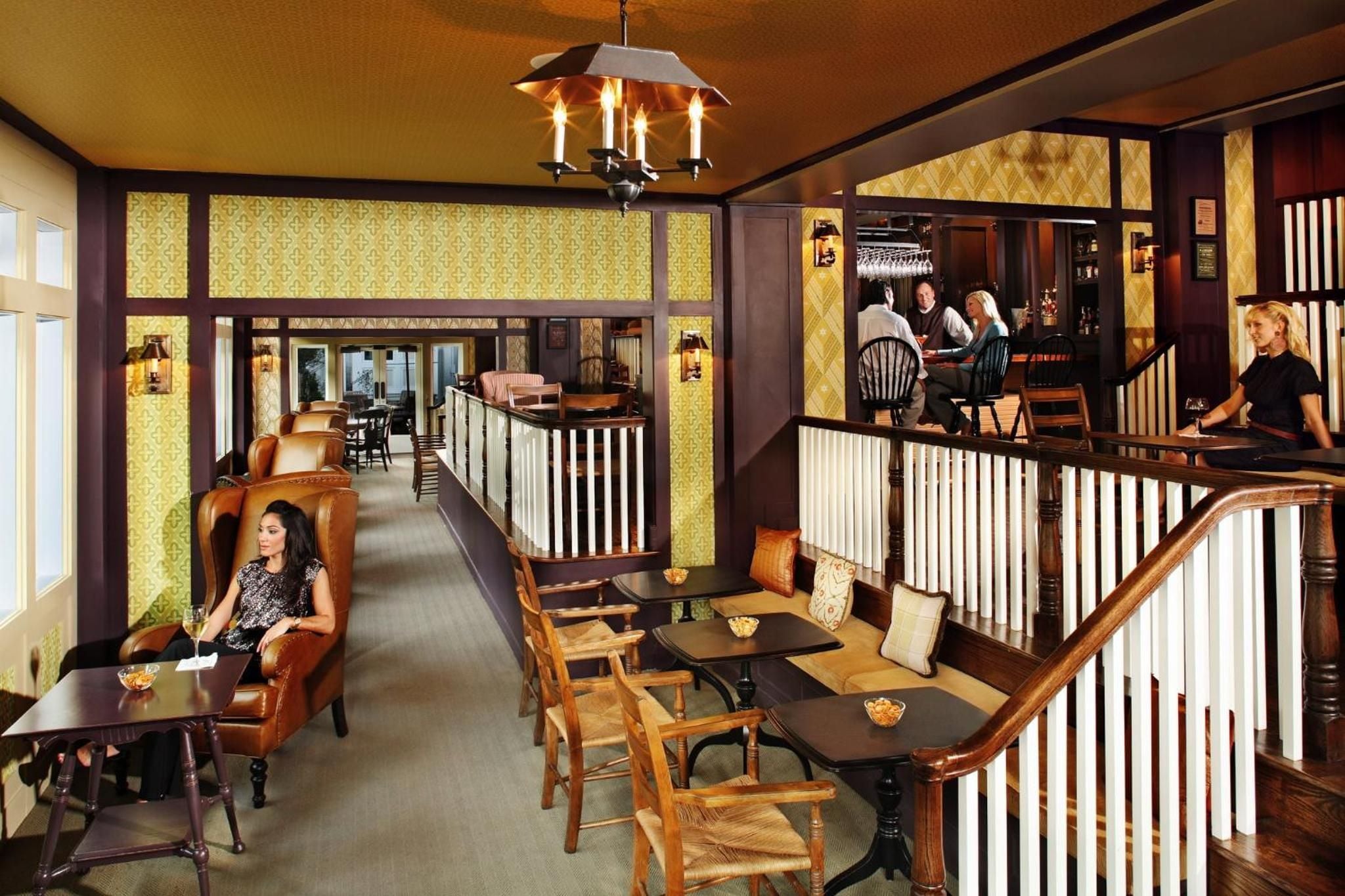 Colonial elegance meets convivial atmosphere in this multi-level tavern, where exposed beams frame intimate seating nooks and golden wallpaper glows beneath wrought-iron chandeliers.