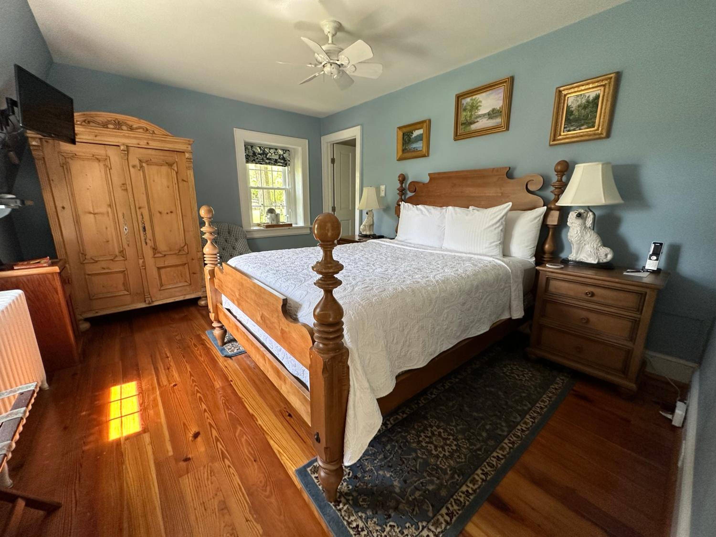Sunlight streams across wide-plank floors in this country-elegant guest room, where handcrafted pine furniture and soft blue walls create an intimate retreat steeped in Virginia charm.
