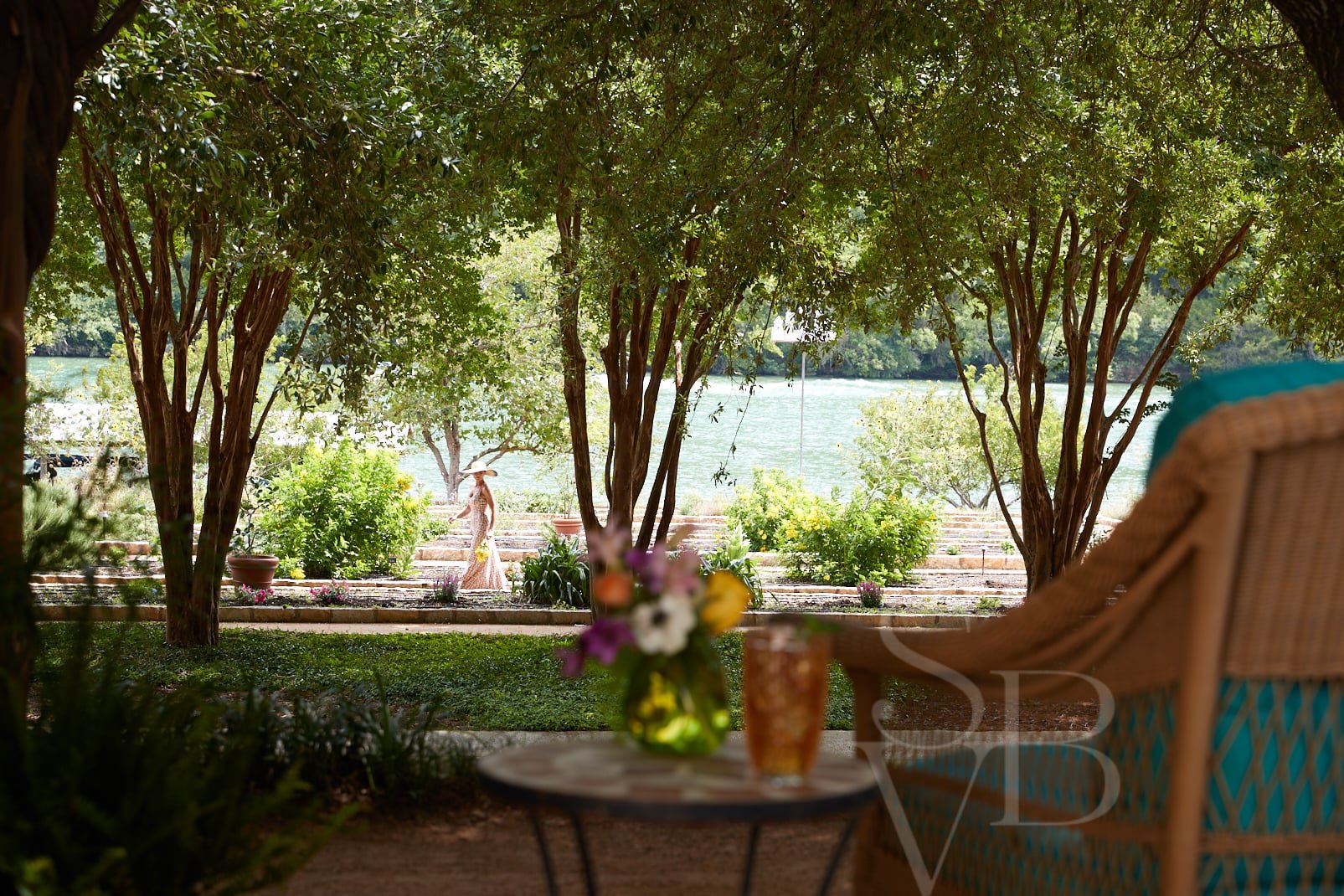 Beneath towering crepe myrtles, a peaceful lakefront terrace invites afternoon contemplation with iced tea and wildflowers, while Lake Austin's gentle waters shimmer beyond manicured gardens.