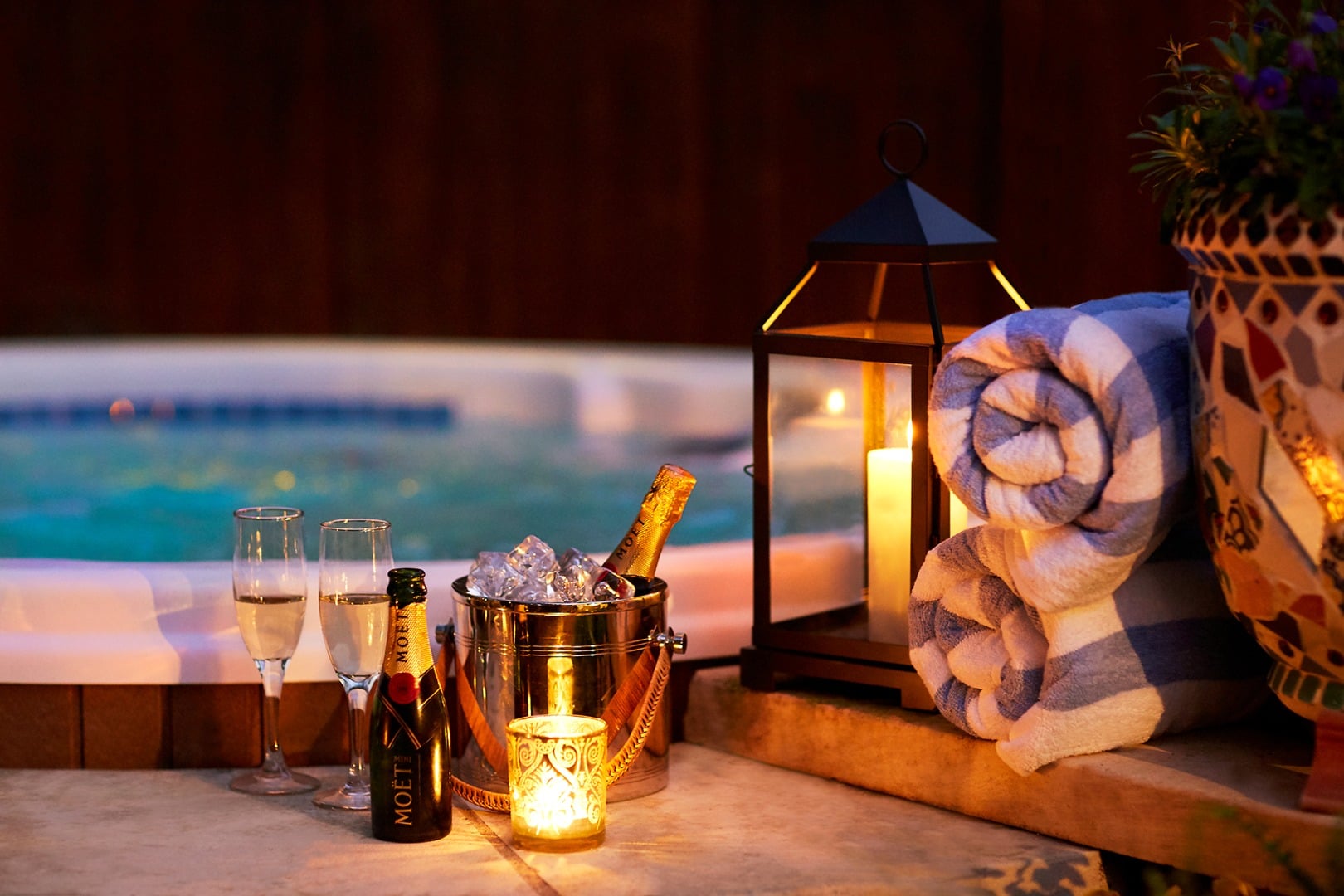 Champagne chills in copper buckets beside flickering lanterns as twilight transforms the poolside into an intimate sanctuary of warm candlelight and luxury.