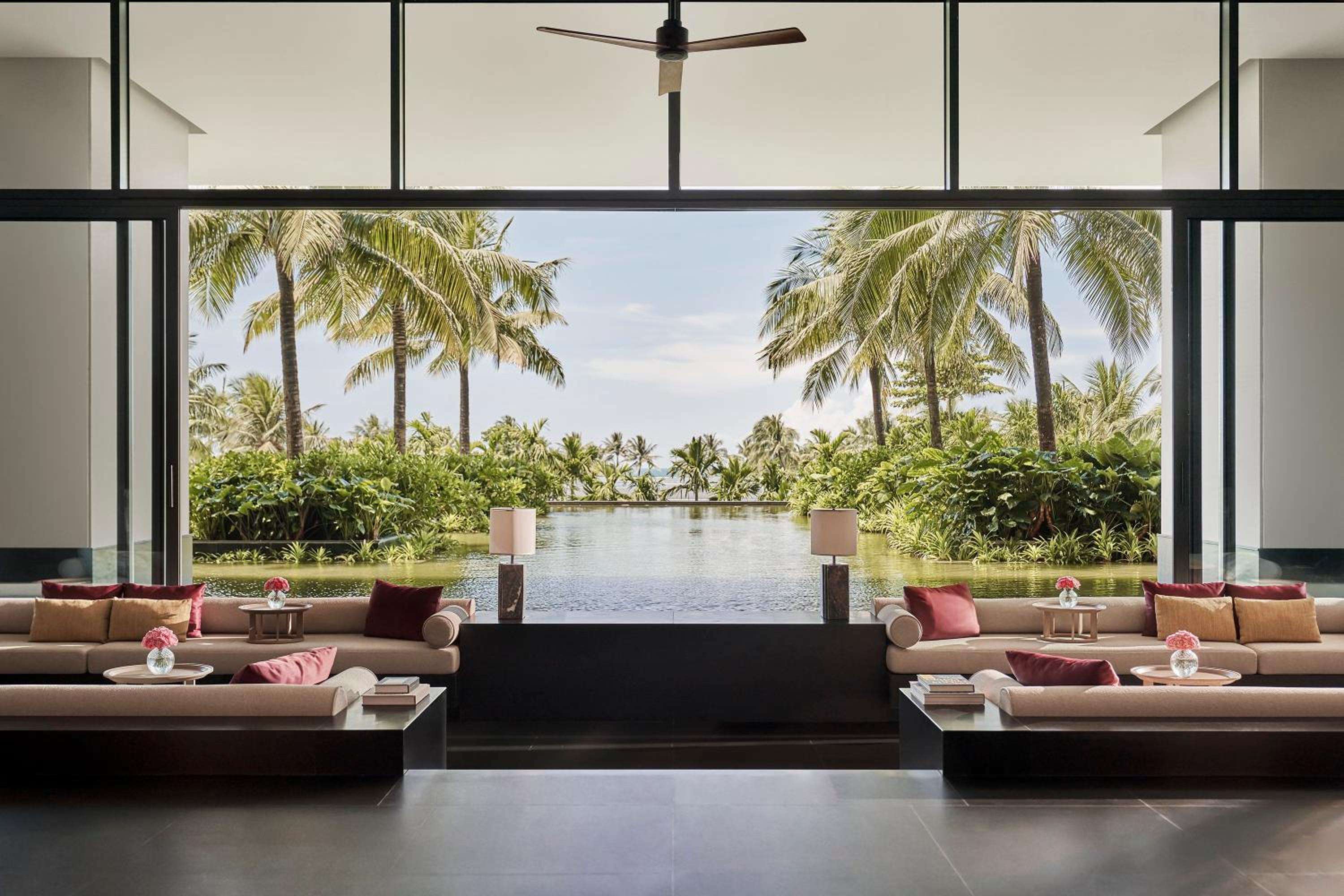 Floor-to-ceiling windows frame swaying palms and infinity pools from the resort's sophisticated lobby, where coral-hued cushions invite lingering over the tropical panorama.