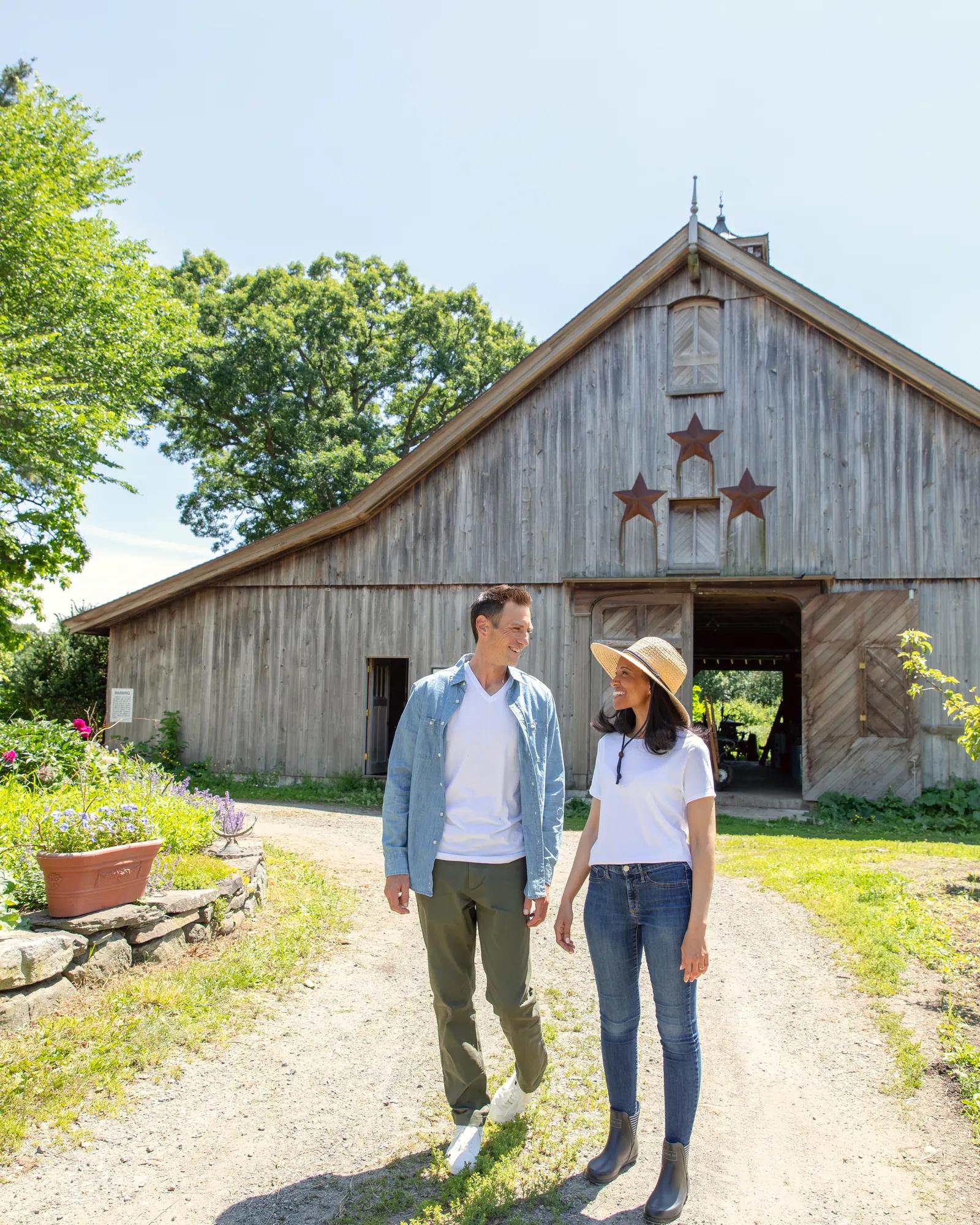 Guests stroll past weathered barn siding adorned with rustic stars, where heritage architecture meets manicured gardens in this quintessentially New England pastoral setting.