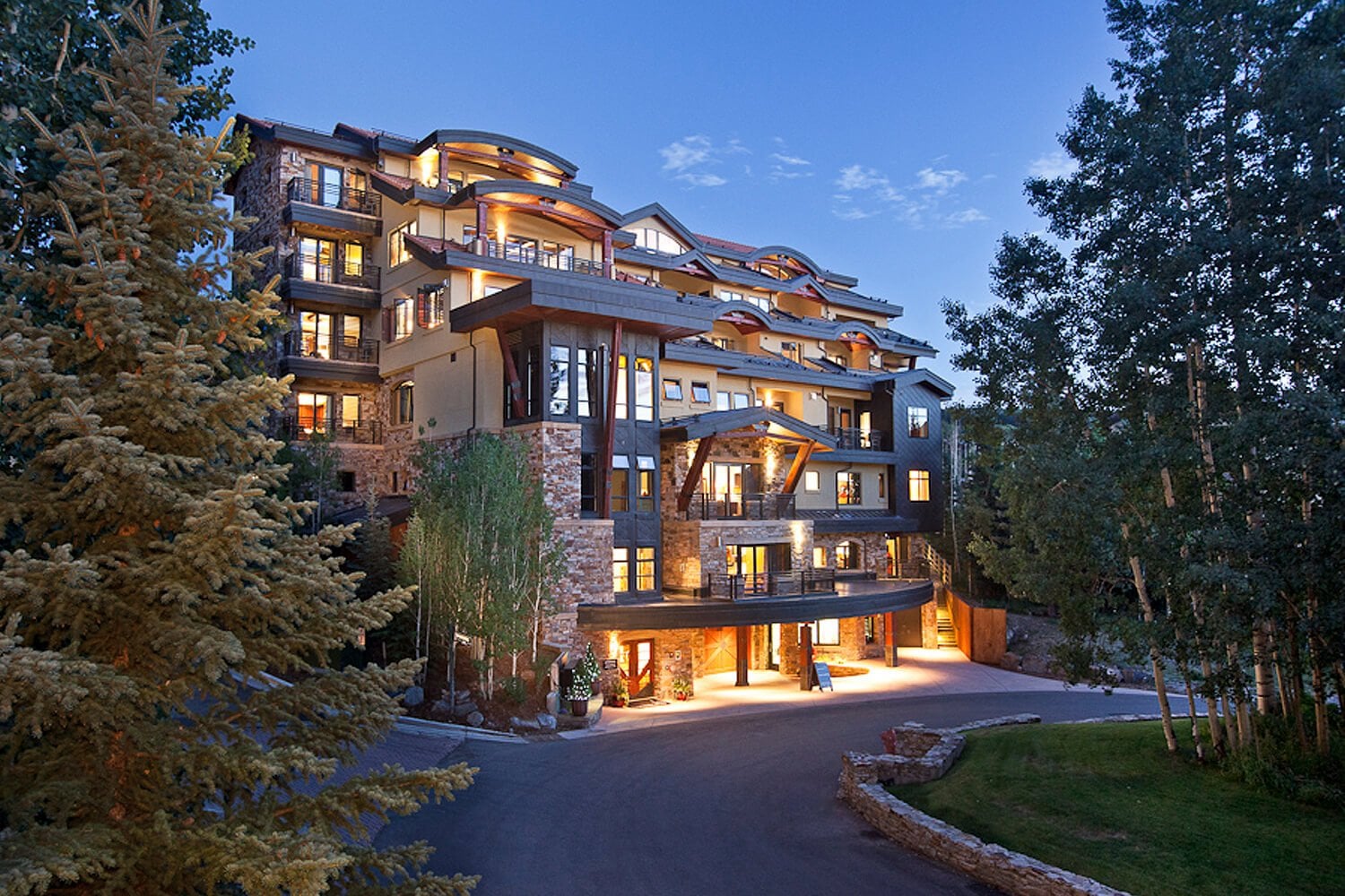 Warm lights spill from timber and stone balconies as this mountain retreat emerges from evergreen forests, its curved architecture following the natural contours of the Colorado hillside.