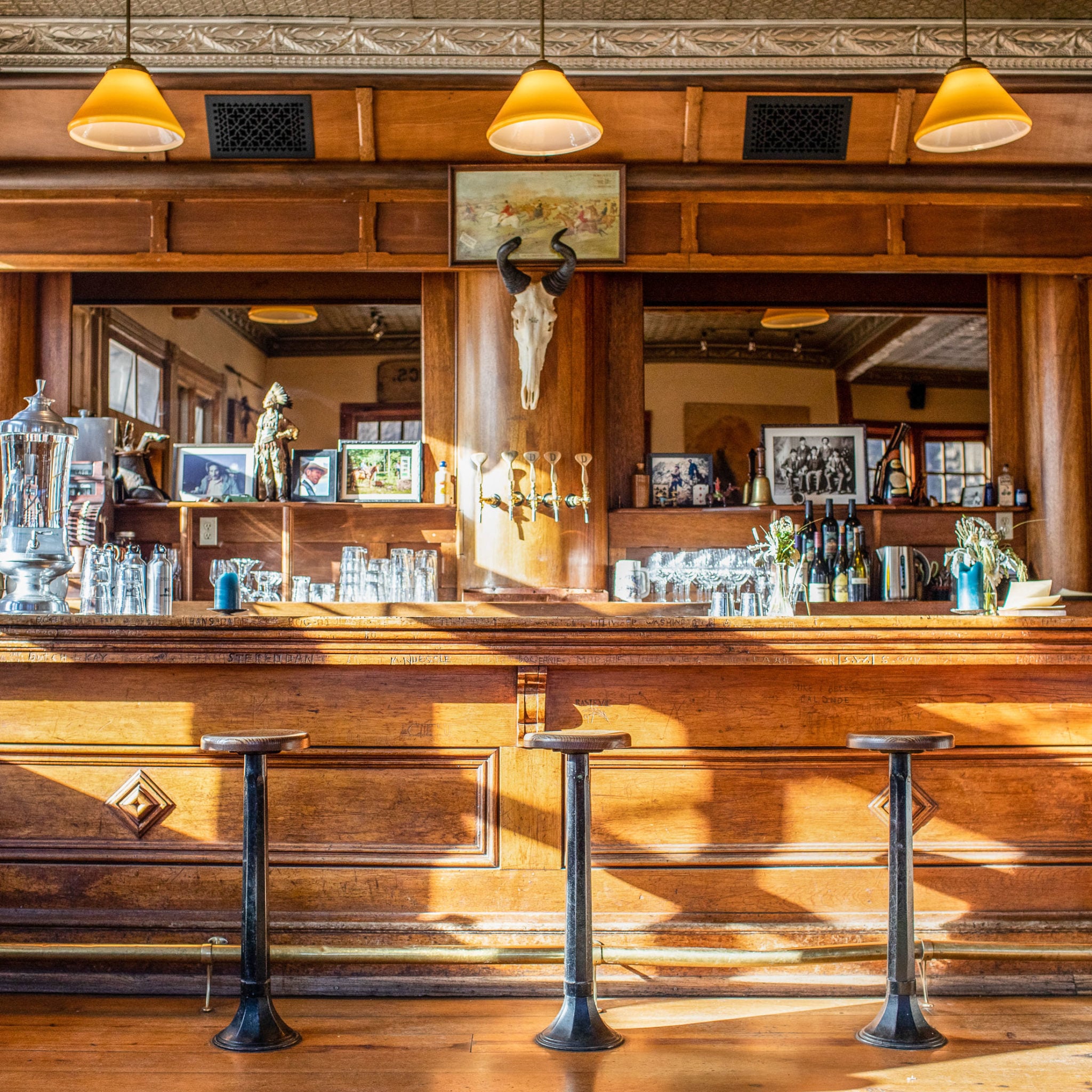Rustic elegance defines the saloon-style bar, where weathered wood, vintage pendant lights, and a mounted cattle skull create an authentic Western atmosphere perfect for evening cocktails.