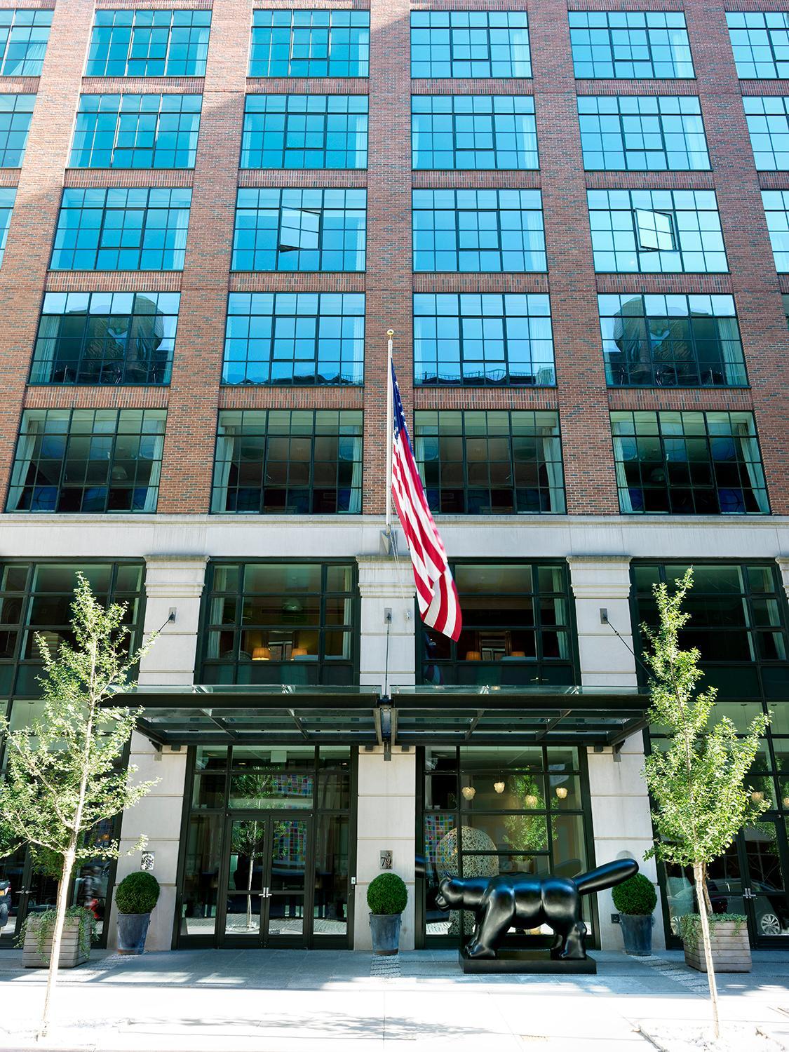 Red brick facade meets polished limestone at street level, where a striking bronze sculpture guards the glass-fronted entrance beneath crisp American flag.