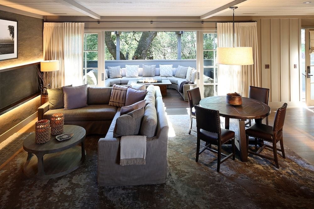 Warm wood beams and plush sectionals create an inviting retreat where guests gather around the fireplace, with treetop views framing intimate conversations over wine.