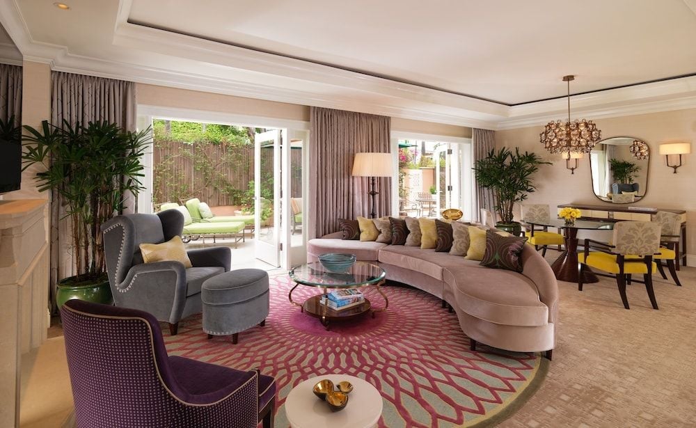 Curved blush velvet seating and jewel-toned accents create an intimate conversation area in this light-filled suite, where French doors reveal a private garden retreat.