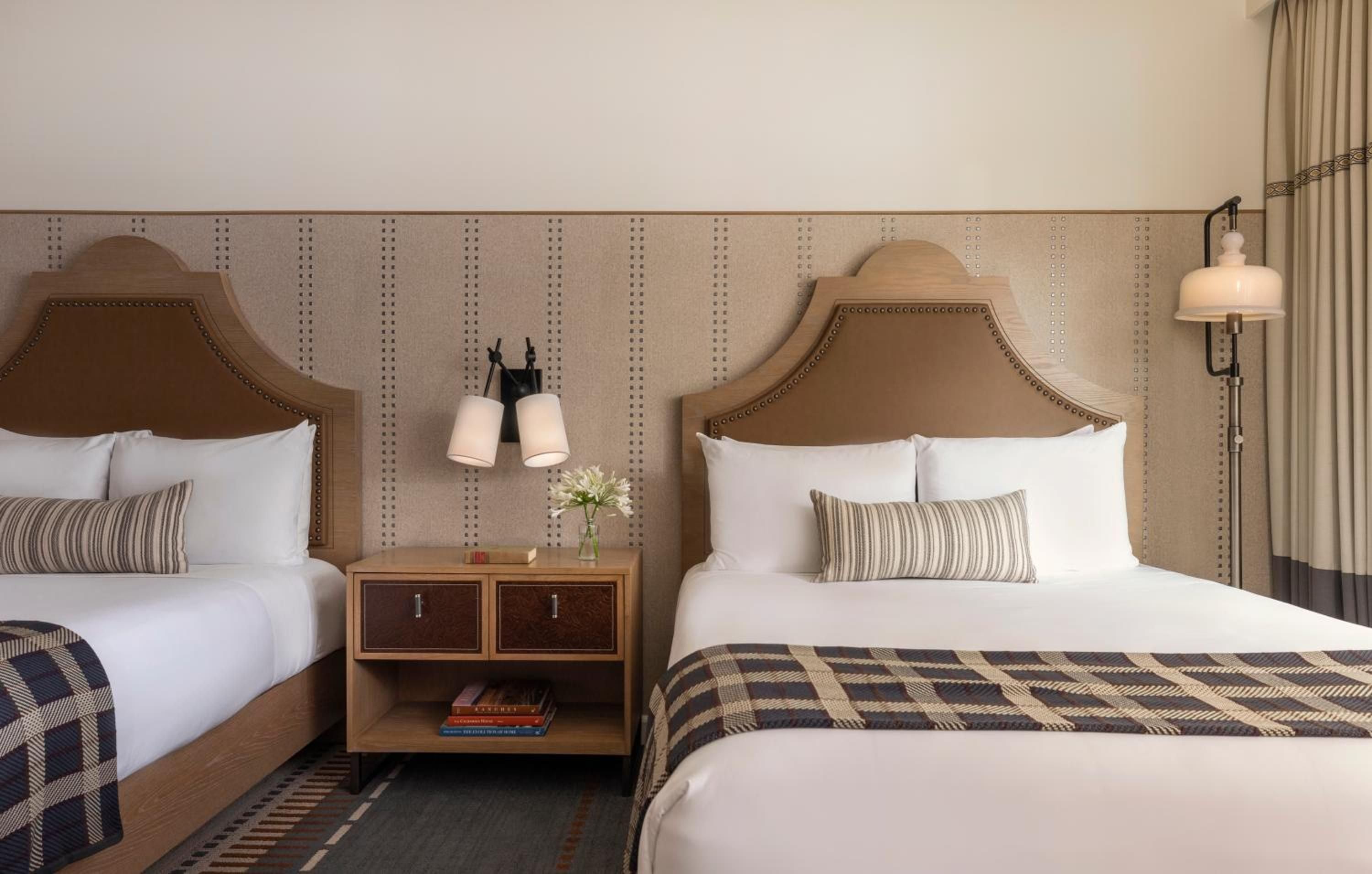 Twin beds wrapped in crisp white linens and plaid throws create a cozy retreat, with warm leather headboards and pendant lighting adding refined ranch elegance.