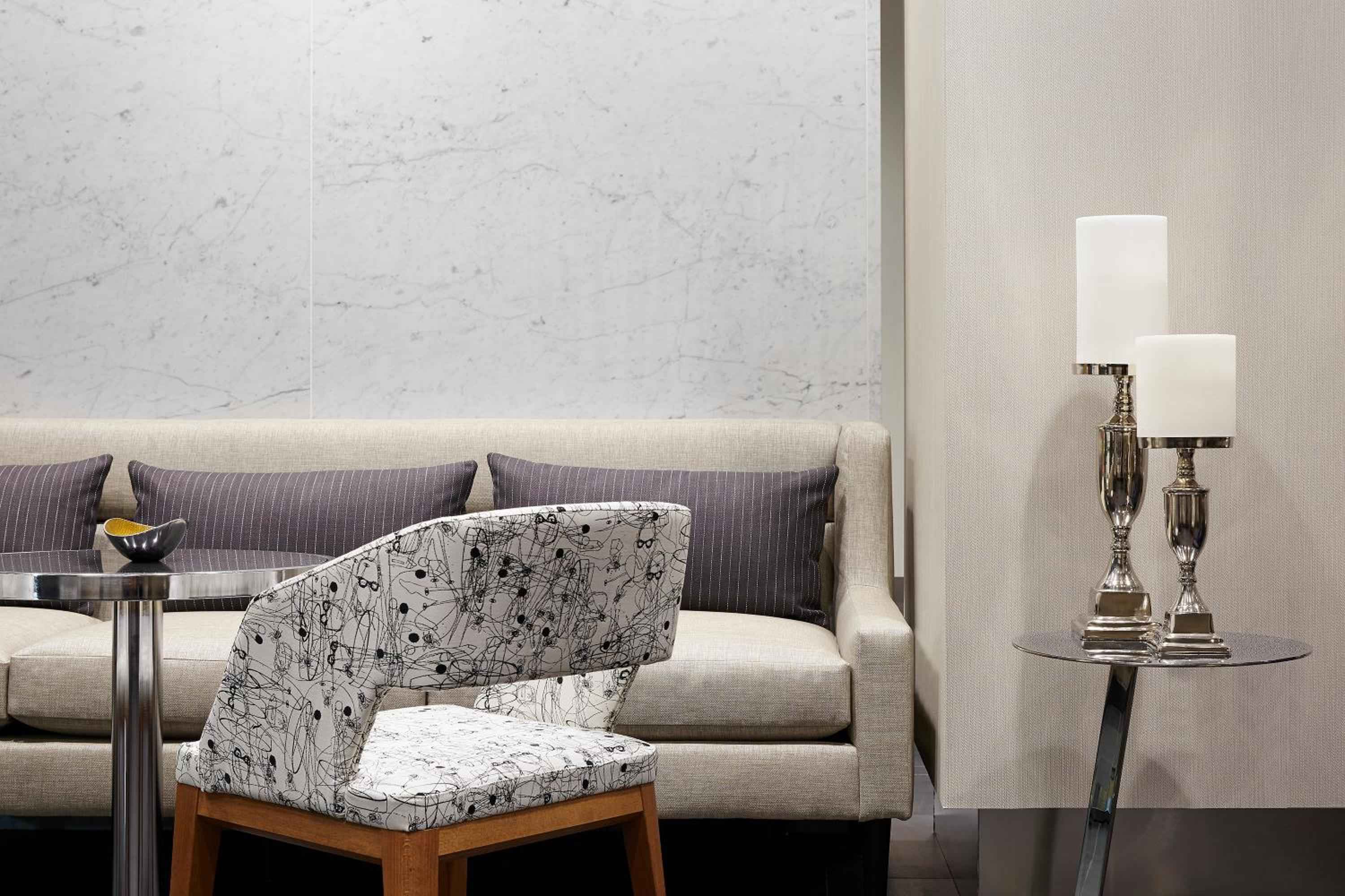 Sophisticated neutral tones and marble accent walls create an intimate seating area where abstract-patterned chairs complement sleek metallic side tables and crystal candlesticks.