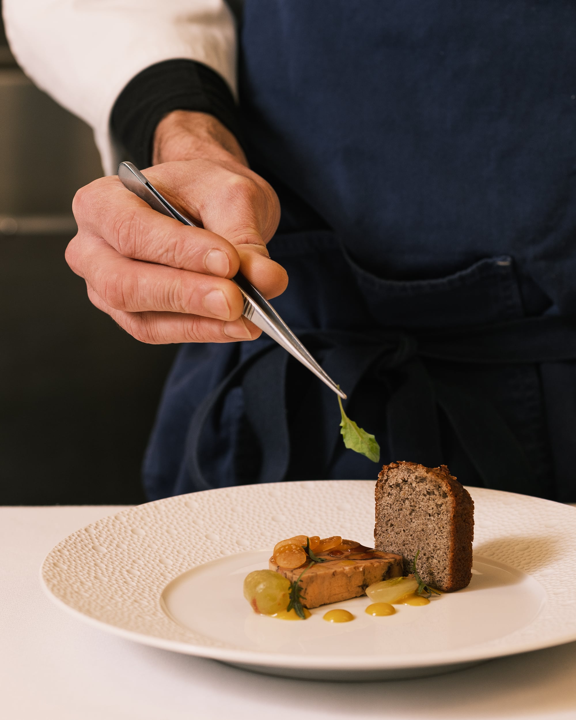 A chef's steady hand delicately places microgreens atop artfully plated cuisine, showcasing the meticulous attention to culinary craft that defines each memorable meal.