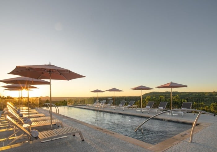 Golden hour light bathes the infinity pool deck, where sleek loungers and umbrellas frame sweeping views of Wimberley's rolling Texas Hill Country.