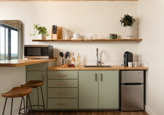 Sage-green cabinetry and warm wood countertops create an inviting kitchenette where morning coffee feels like a ritual worth savoring.