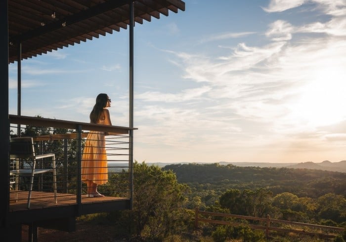 Golden hour bathes a guest in warm light as she gazes across the rolling Texas Hill Country from her private deck, where modern architecture meets untamed wilderness.