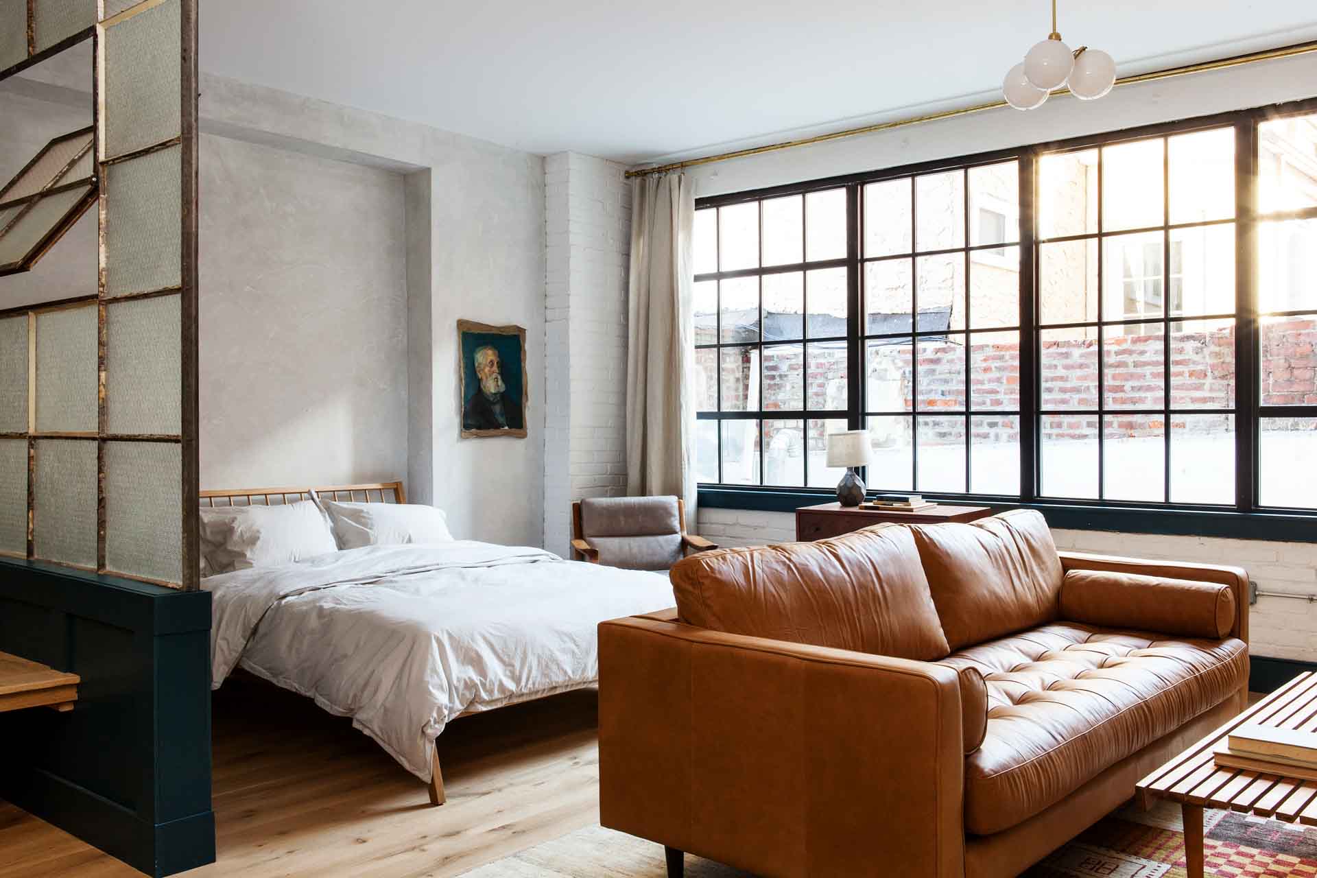 Industrial elegance defines this loft-style suite, where cognac leather meets exposed brick and steel-framed windows flood hardwood floors with golden afternoon light.