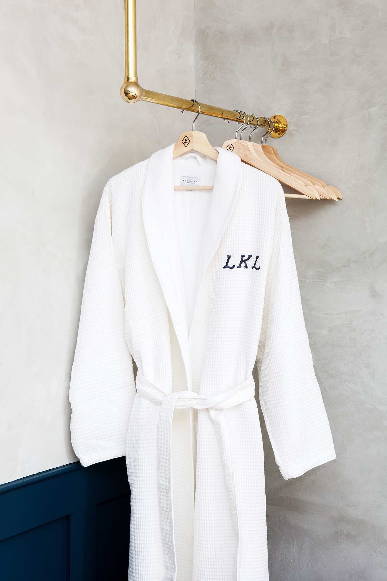 Monogrammed waffle-weave robes hang from gleaming brass fixtures, embodying the thoughtful luxury that defines every corner of this meticulously designed boutique property.