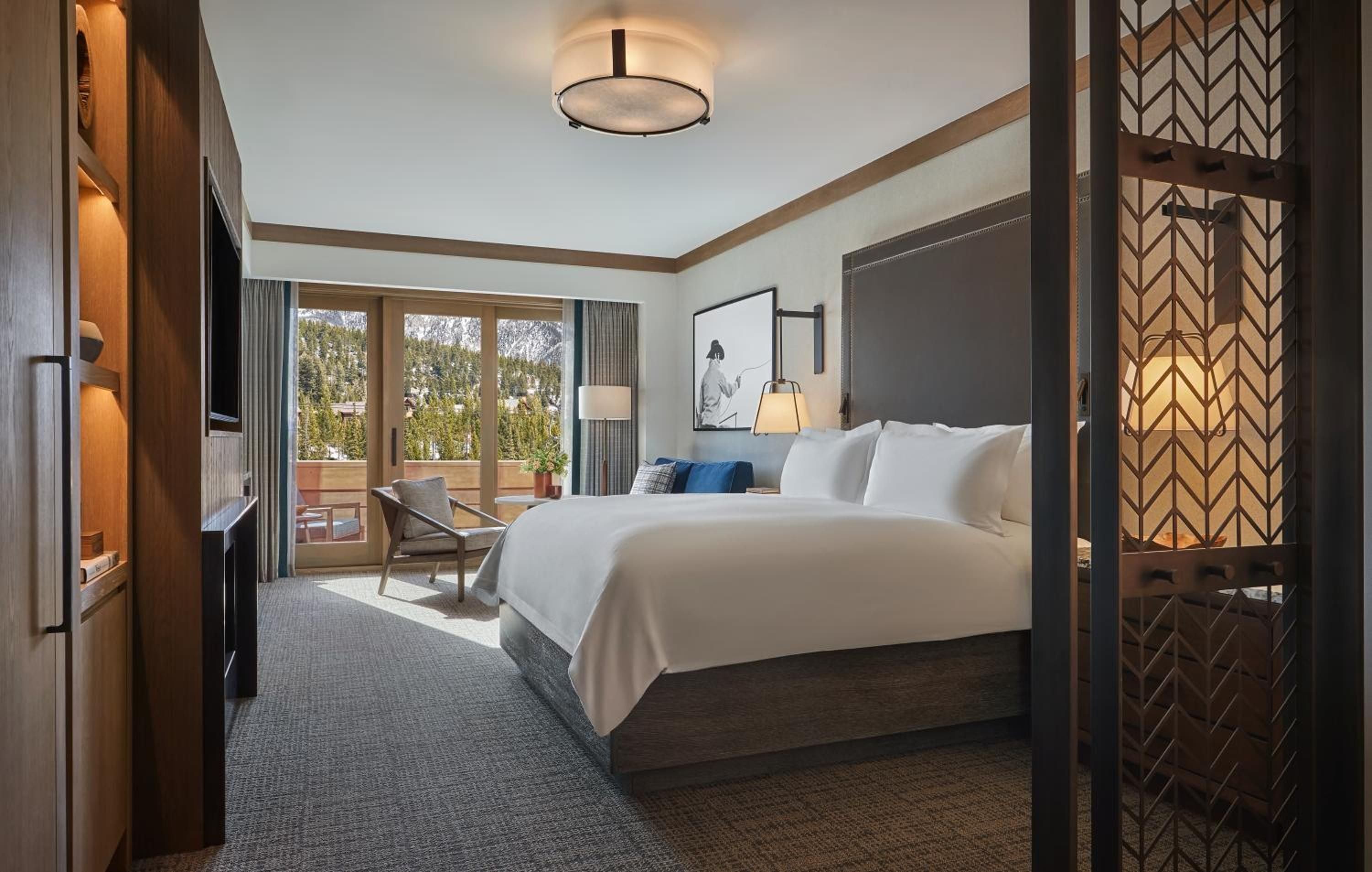 Warm wood tones and geometric screens frame crisp white linens, while mountain views beyond the balcony promise alpine adventures from this thoughtfully appointed retreat.