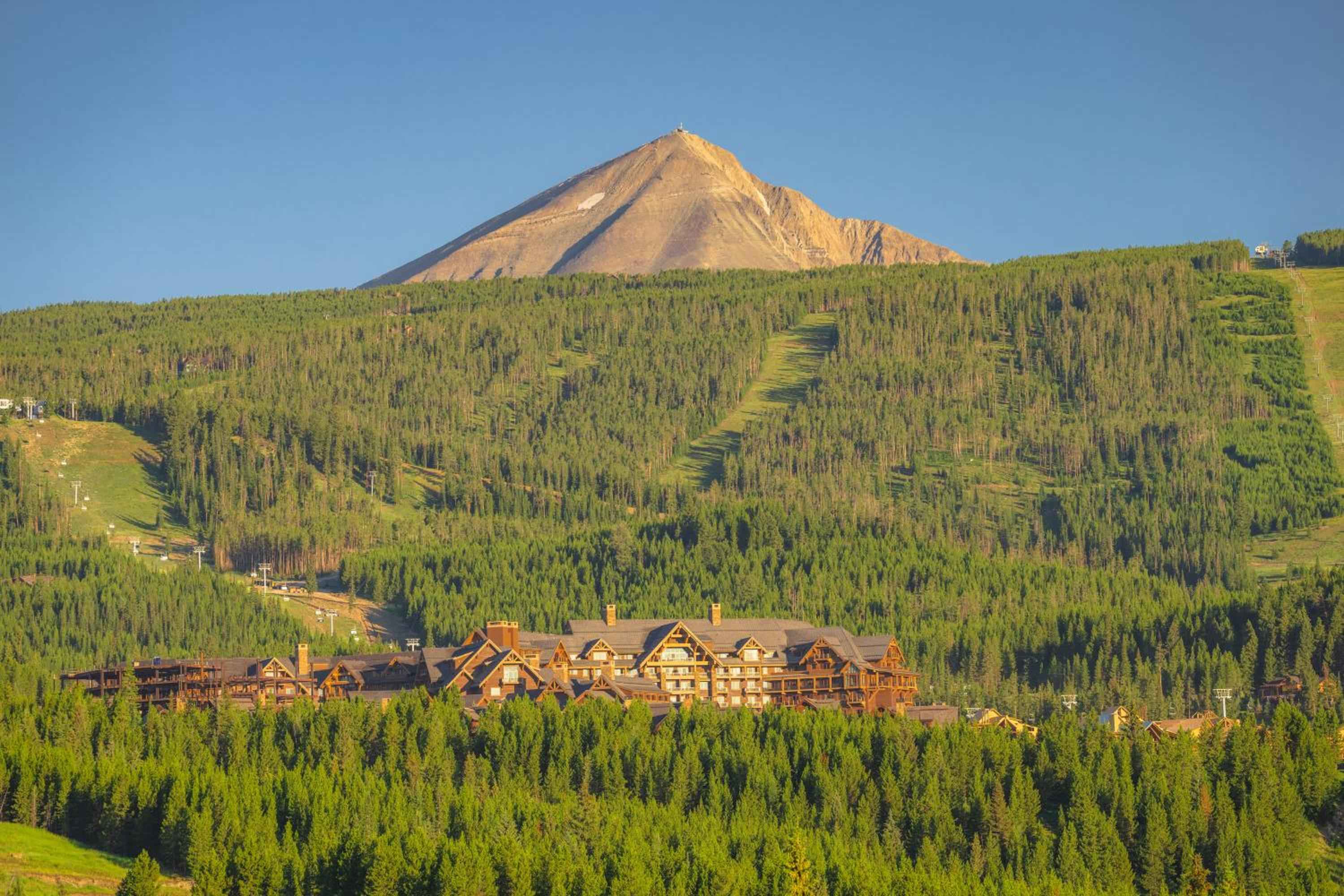 Golden hour light bathes the lodge's timber architecture as Lone Peak towers majestically beyond forested slopes carved with summer ski runs.