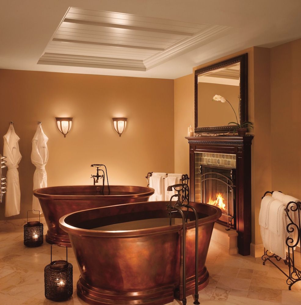 Copper soaking tubs catch firelight in this sumptuous bathroom retreat, where warm amber walls and flickering candles create an intimate sanctuary for après-ski relaxation.