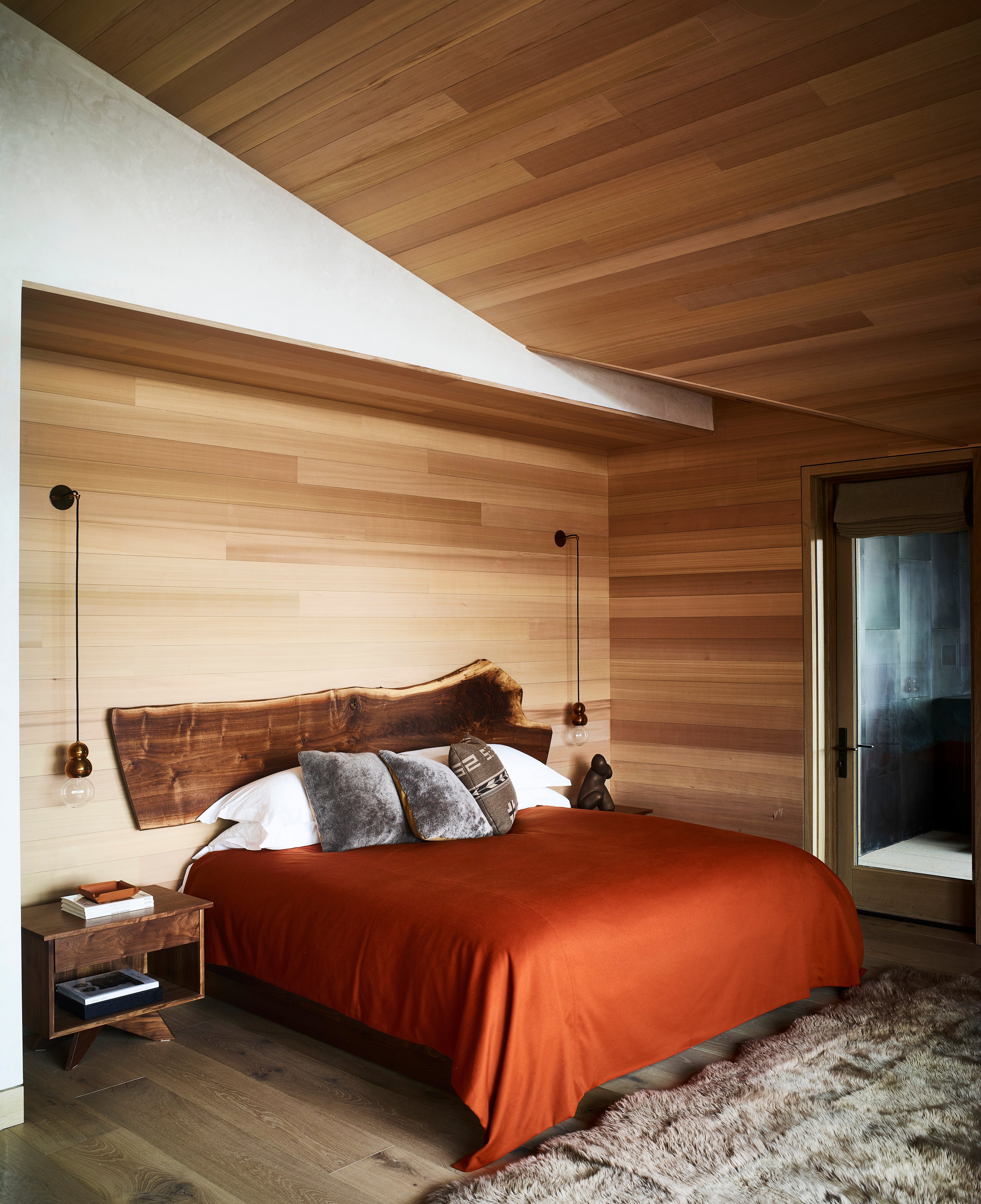 Raw-edge wood headboards and burnt orange linens create intimate mountain sanctuary beneath cedar-planked ceilings, where pendant lights cast warm pools of light over natural textures.