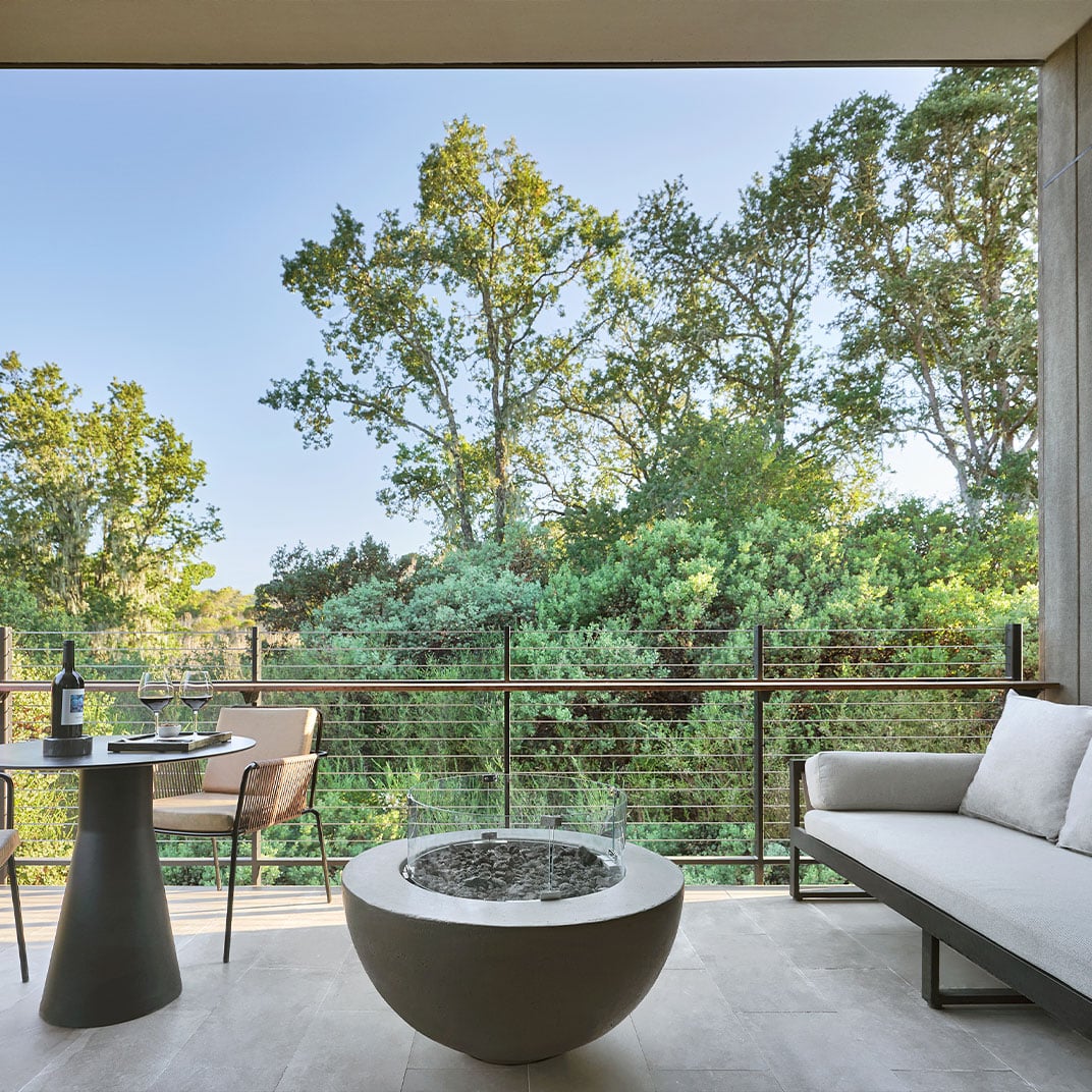 Wine glasses catch golden light on this secluded terrace, where a sculptural fire bowl anchors intimate moments overlooking Sonoma's verdant canopy.