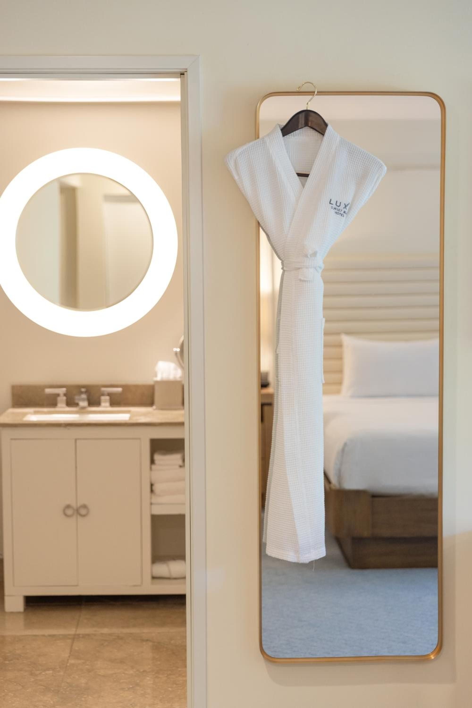 Waffle-weave robes hang beside illuminated vanity mirrors, where warm lighting and neutral tones create a spa-like sanctuary for morning rituals.