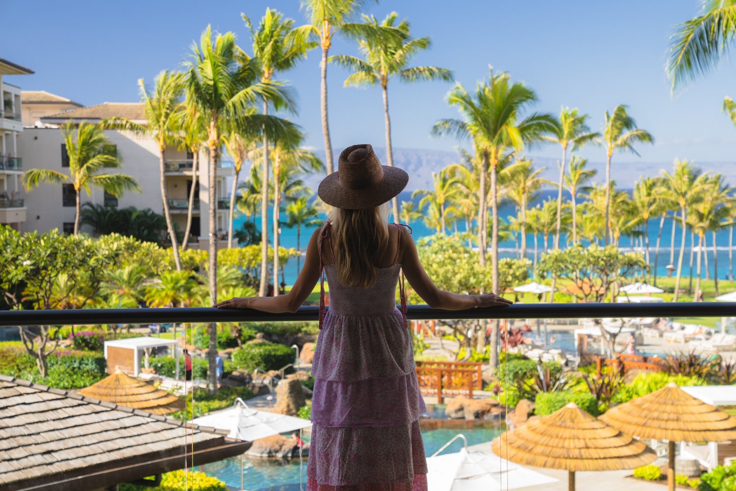 From a private balcony, palm fronds frame the azure Pacific while golden thatched umbrellas dot the infinity pool below, creating quintessential Maui magic.