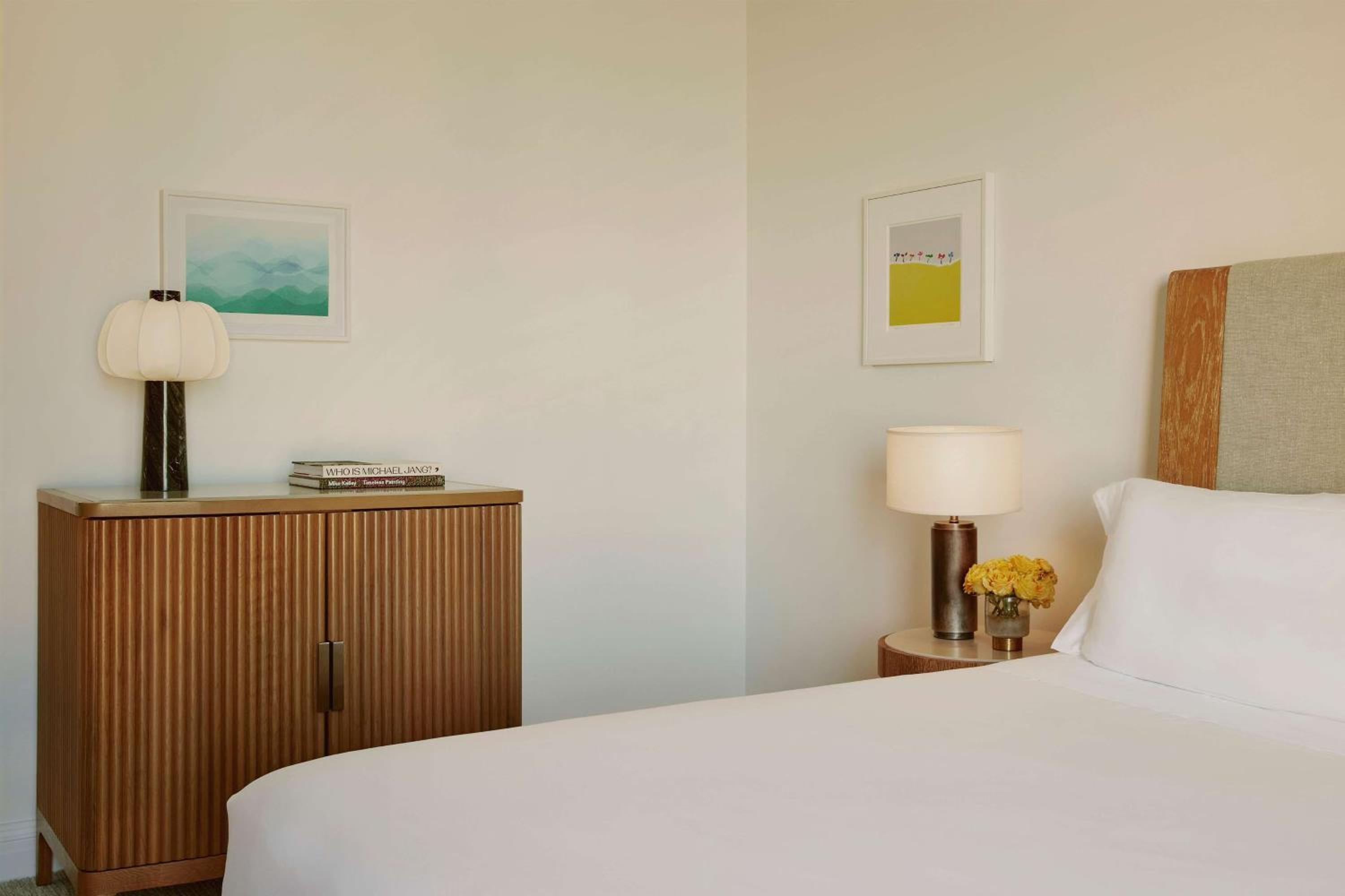 Warm oak furnishings and crisp white linens create a serene sanctuary, where fluted wood credenzas and soft lamplight evoke mid-century California sophistication.