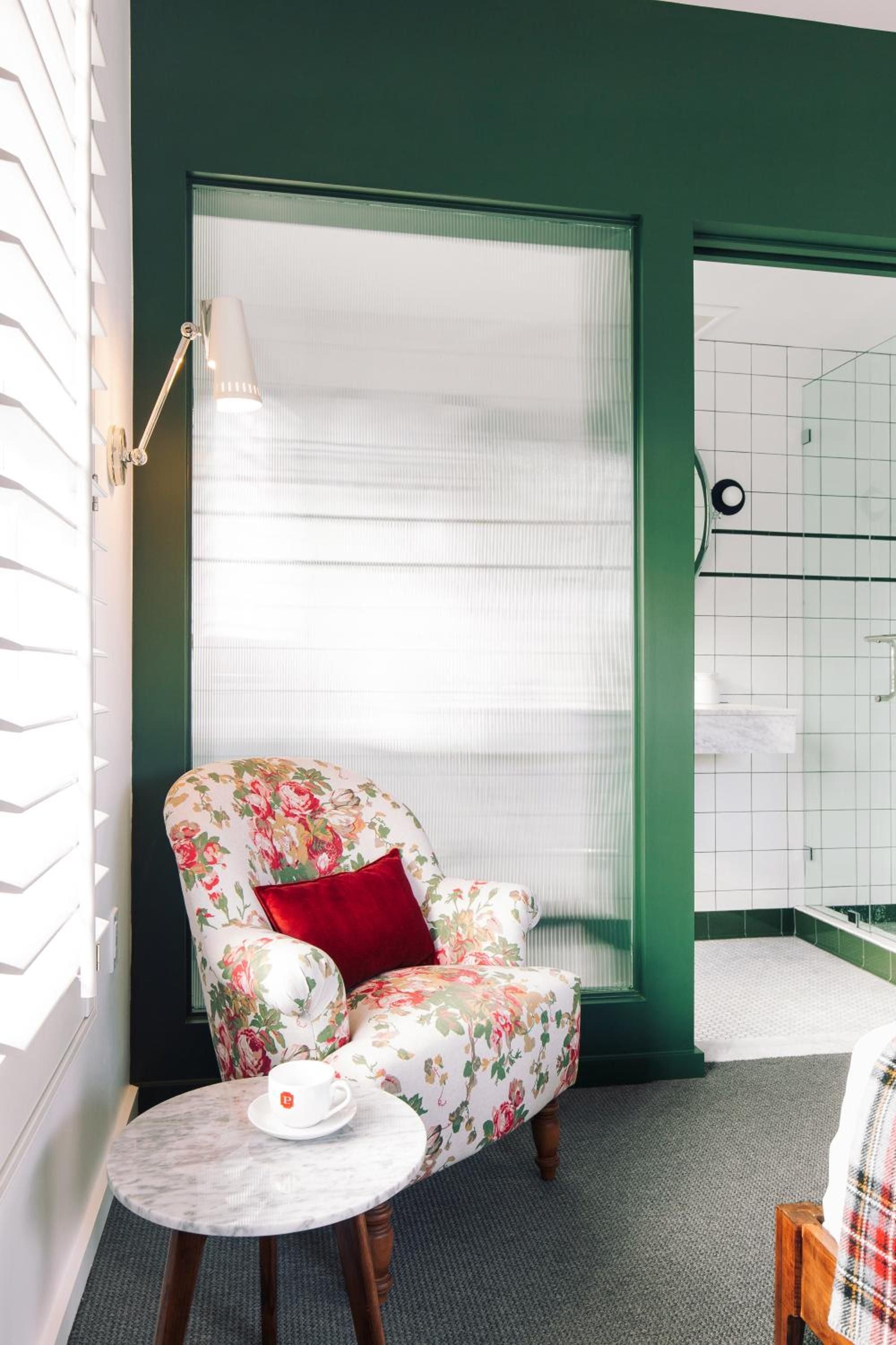 Floral chintz armchair paired with emerald green accents creates an unexpectedly charming corner, where morning coffee feels like a ritual in grandmother's best parlor.