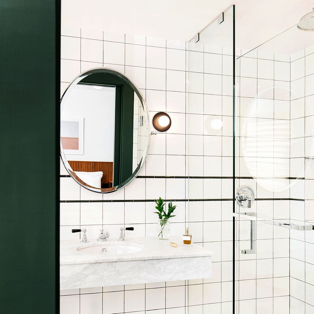 White subway tiles with charcoal grout create graphic lines in this thoughtfully appointed bathroom, where a round mirror and marble vanity add sophisticated contrast.