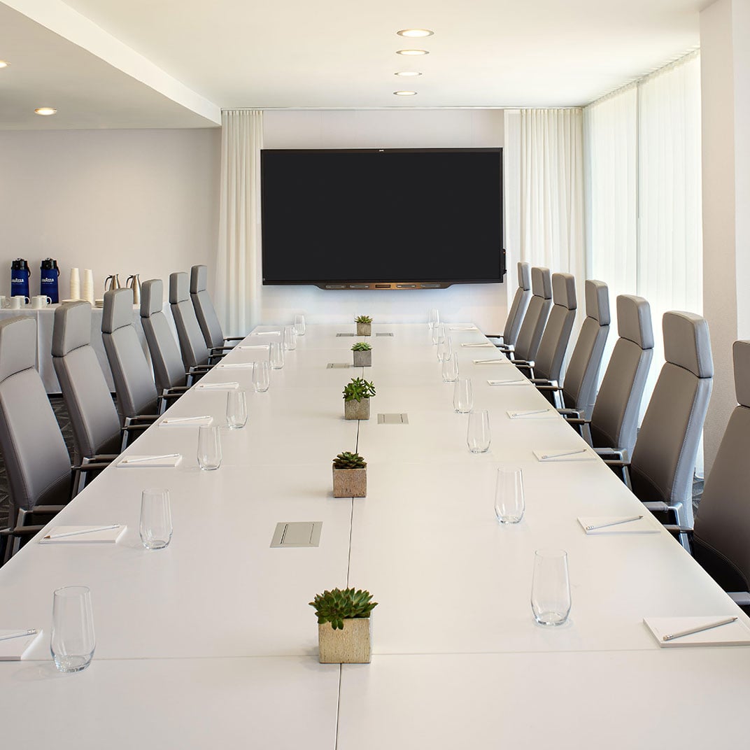 Sleek gray chairs surround pristine white tables dotted with succulents, while floor-to-ceiling windows bathe this boardroom in soft natural light.