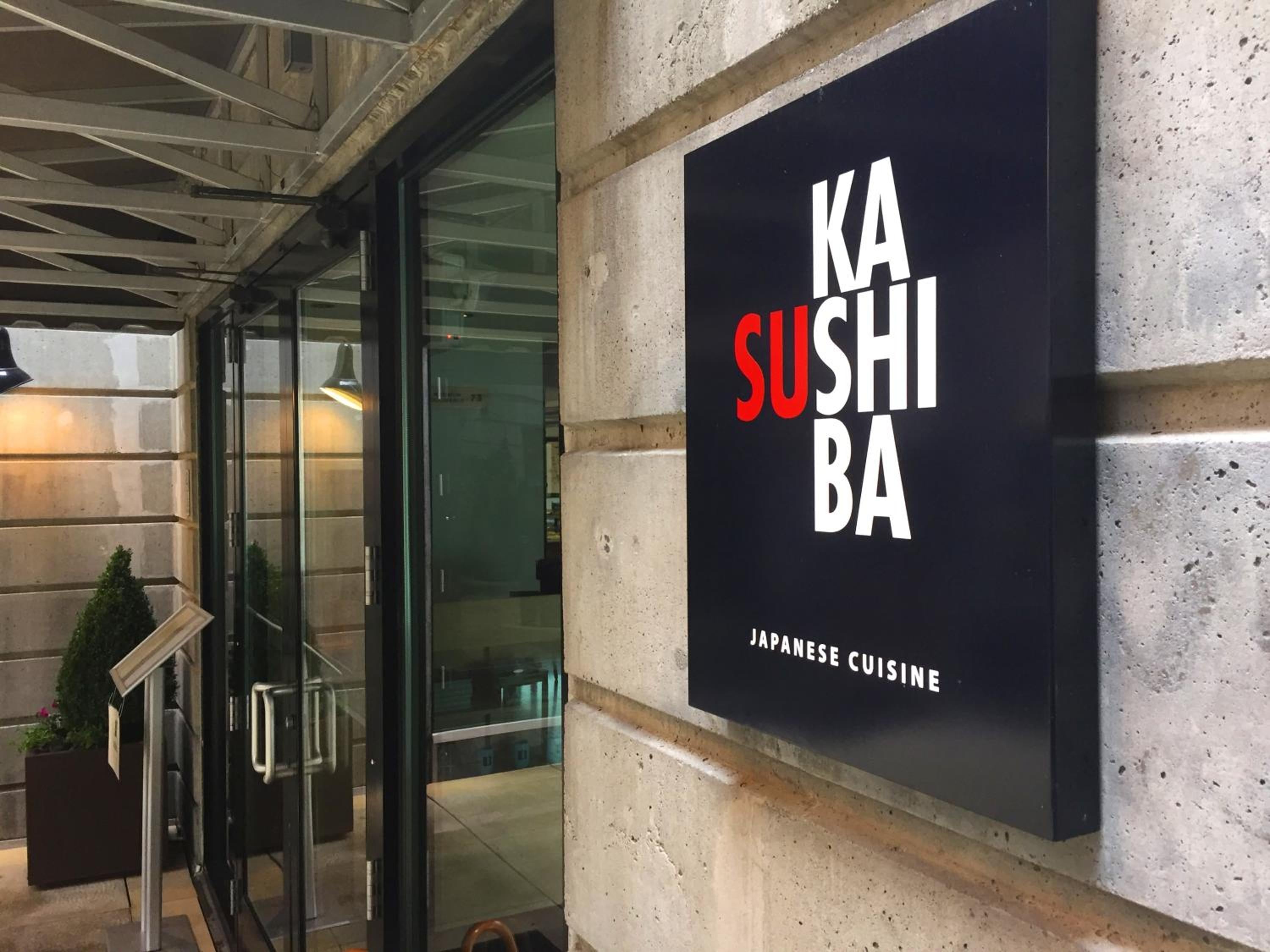 Kashiba's striking black signage against textured concrete walls signals exceptional Japanese cuisine, where fresh sushi awaits behind glass doors in this sophisticated Pike Place Market destination.
