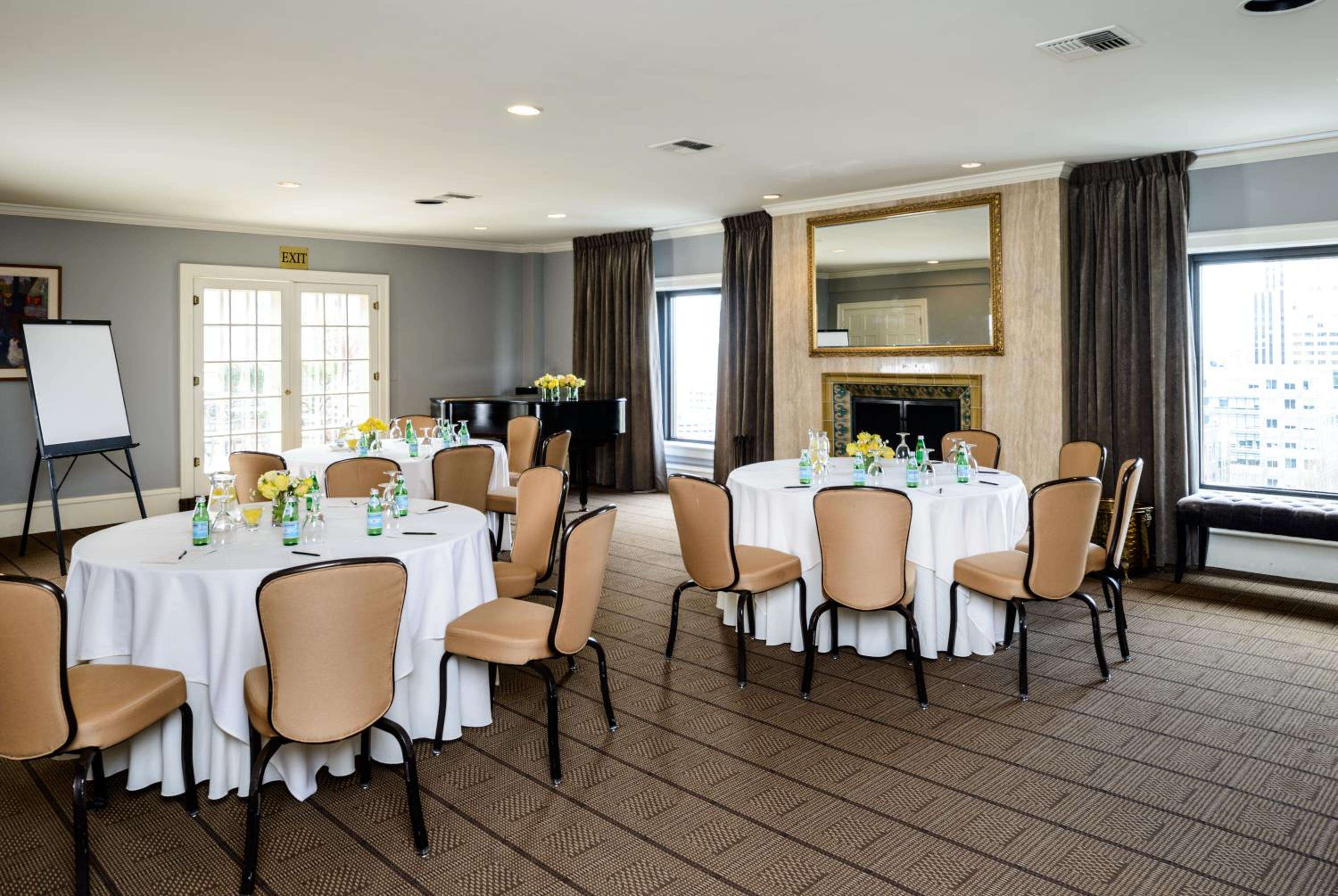 Elegant meeting space features warm tan leather chairs arranged around crisp white linens, while city views and a cozy fireplace create an inviting atmosphere for corporate gatherings.