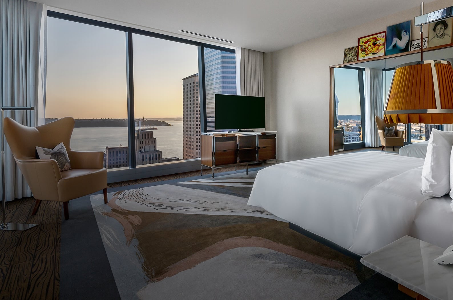 Floor-to-ceiling windows frame Elliott Bay's shimmering expanse while warm amber lighting and contemporary furnishings create an intimate sanctuary high above Seattle's urban canyon.