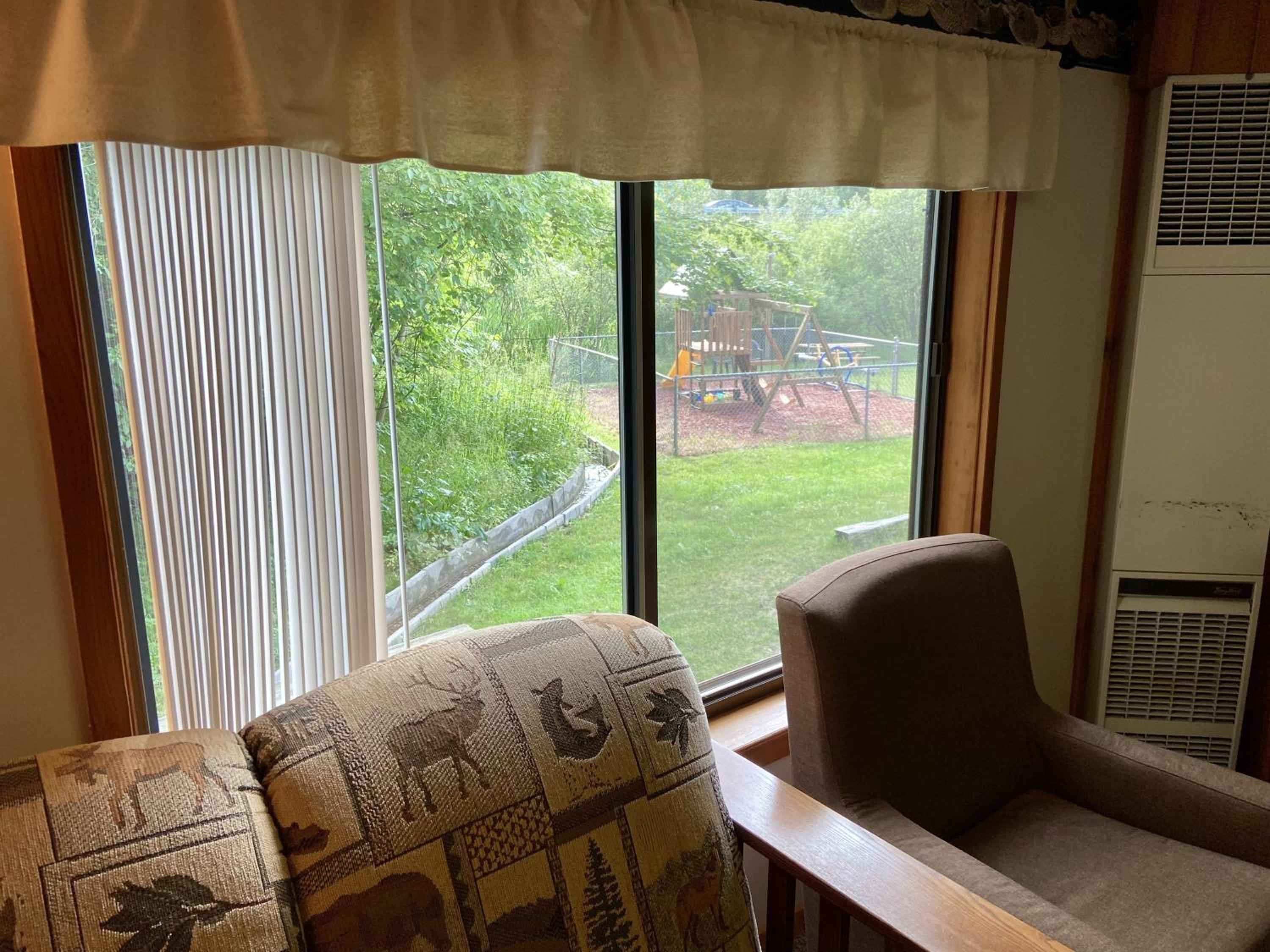 Wildlife-motif chairs frame windows overlooking the playground and gardens, where families gather beneath towering maples and willows at this charming riverside retreat.