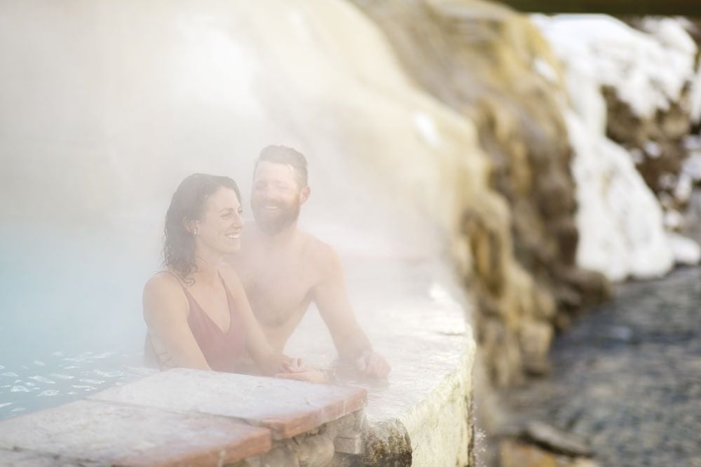 Steam rises from mineral-rich waters as couples find intimate moments in naturally carved stone pools, where ancient rock formations create private sanctuaries for relaxation.