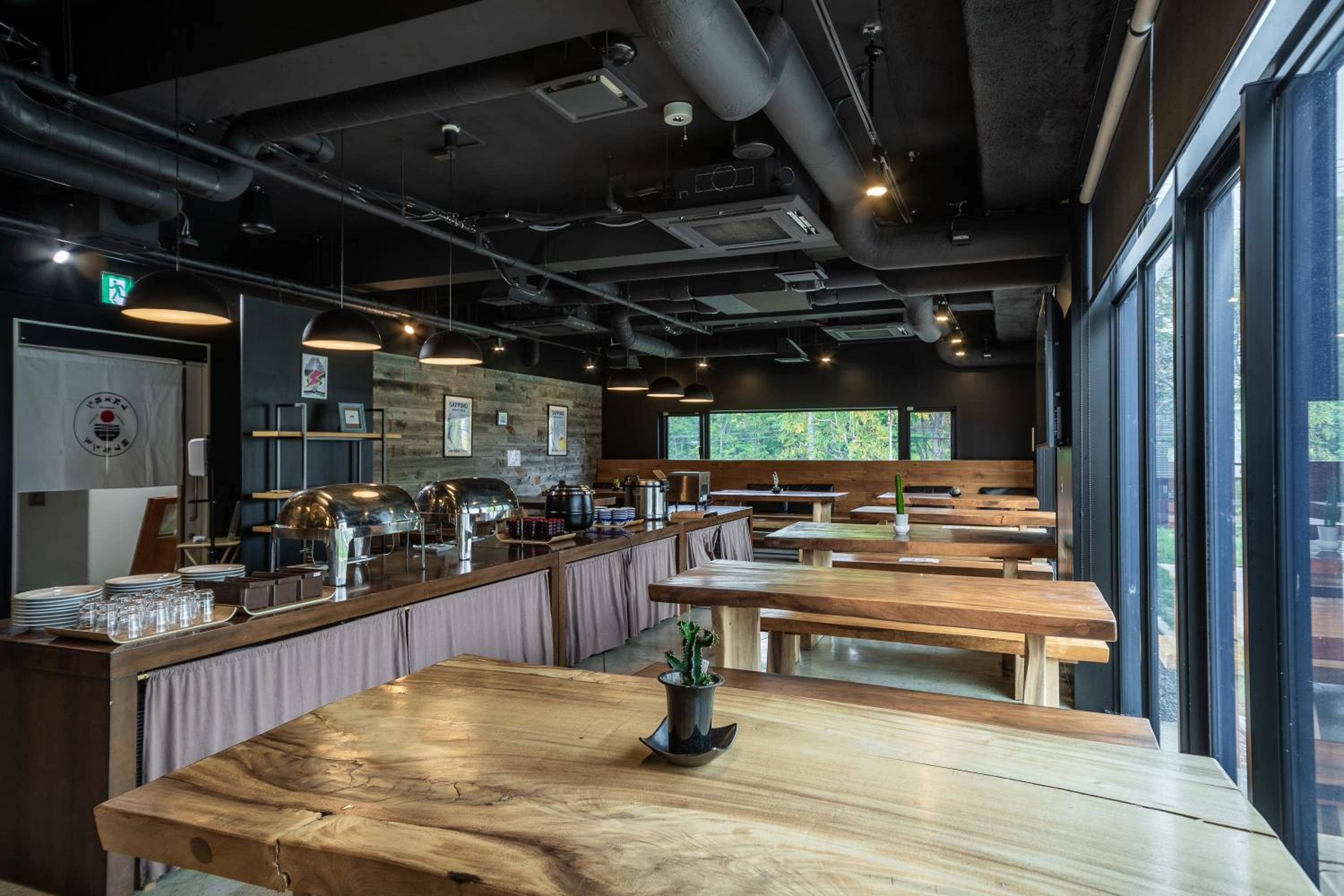 Natural wood tables and exposed industrial ceilings create a modern mountain lodge atmosphere, where breakfast buffet stations invite leisurely mornings overlooking Niseko's verdant landscape.