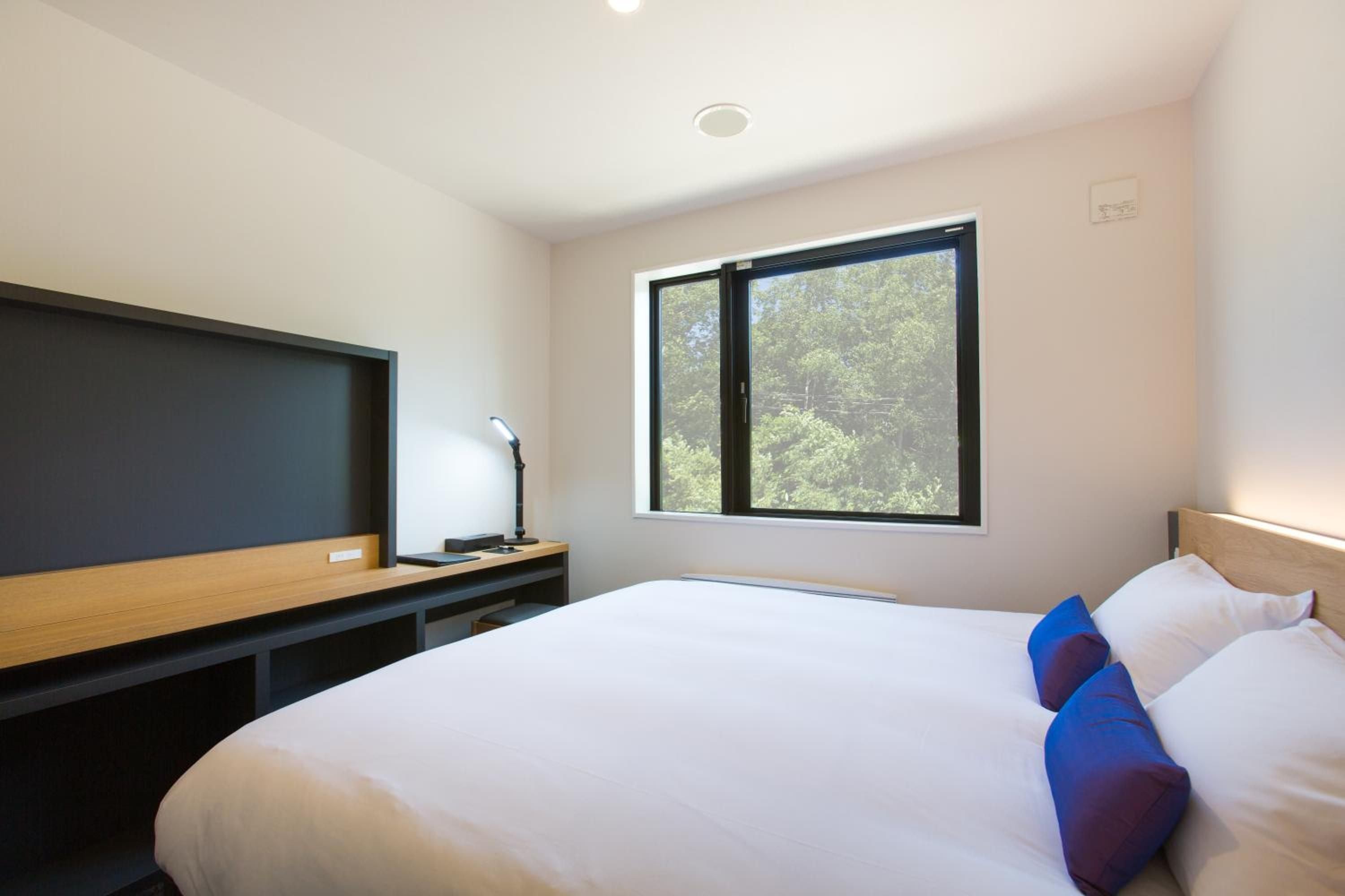 Clean lines and warm wood create a serene sanctuary, while floor-to-ceiling windows frame Niseko's lush forest canopy in this thoughtfully designed guest room.