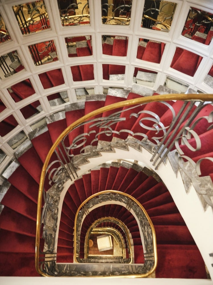 Crimson velvet carpeting winds down the hotel's dramatic spiral staircase, where ornate golden railings and mirrored panels create an enchanting descent through history.