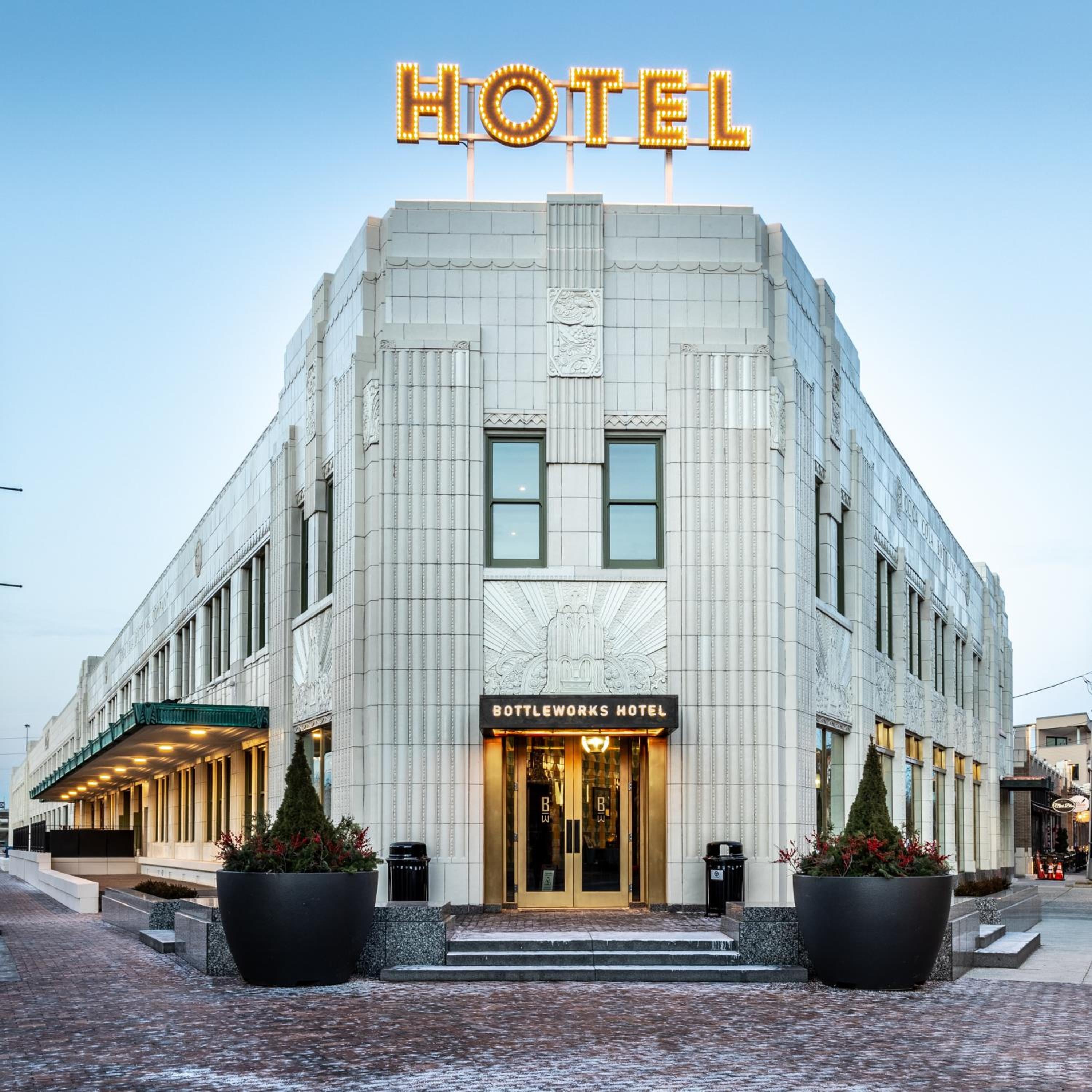 Art Deco grandeur meets modern hospitality where golden marquee letters crown this limestone masterpiece, its illuminated entrance beckoning through Indianapolis's historic Bottleworks district.