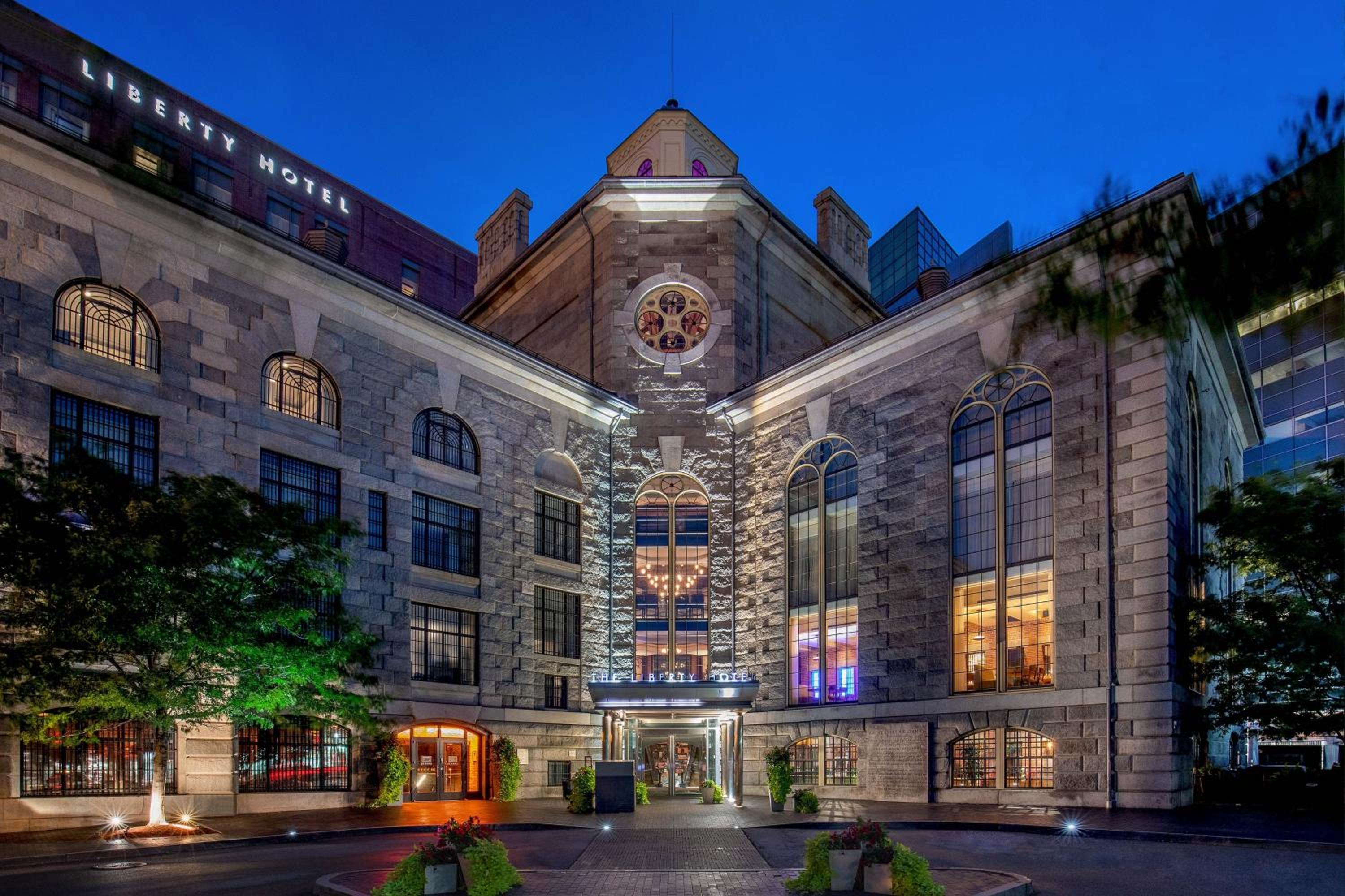 Stone masonry and soaring arched windows create a cathedral-like grandeur at this former jail turned luxury retreat, where history meets hospitality beneath Boston's twilight sky.