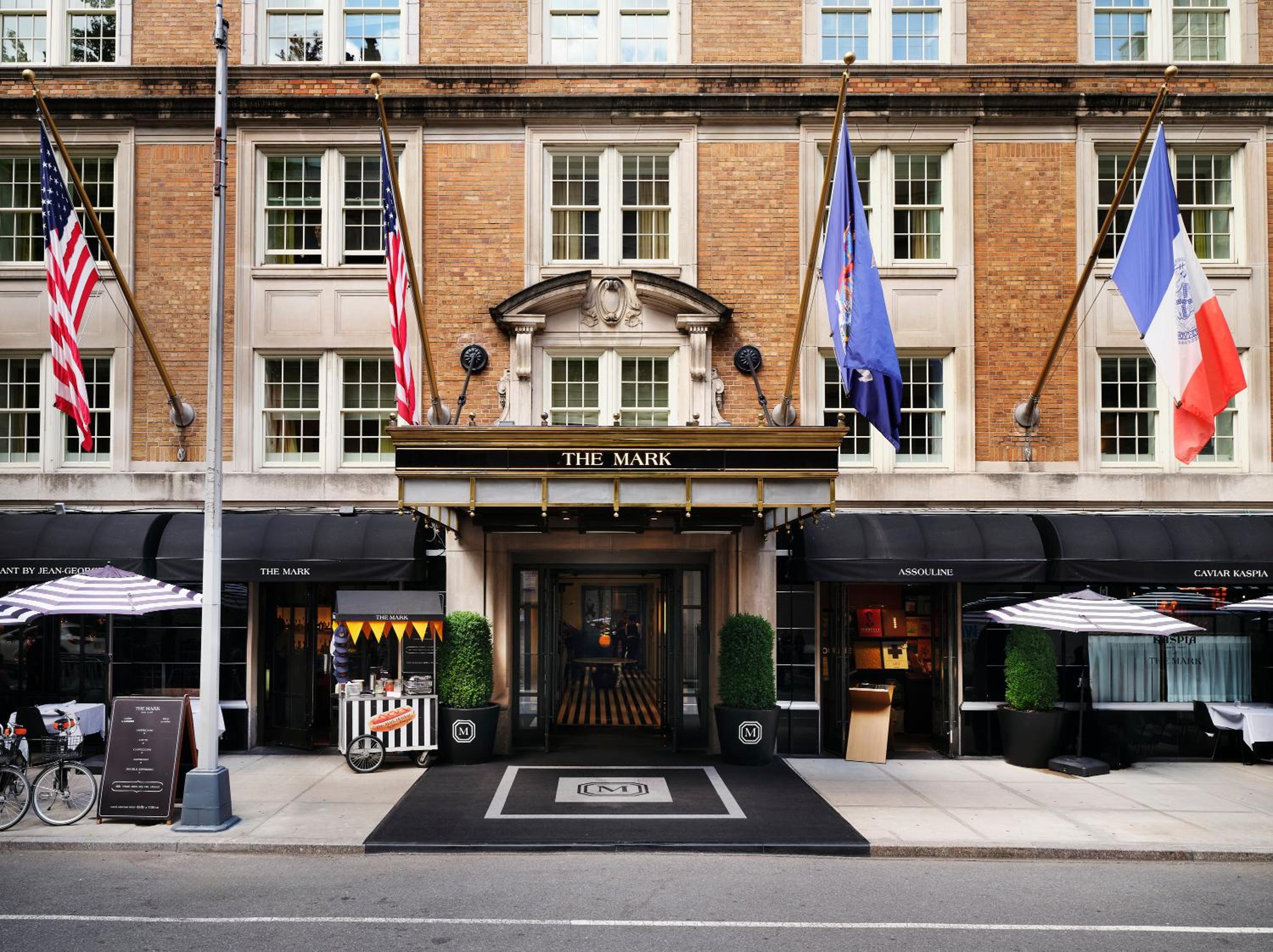 Classic red brick facade adorns this Upper East Side sanctuary, where international flags flutter above gleaming black awnings and a welcoming entrance mat beckons discerning guests inside.