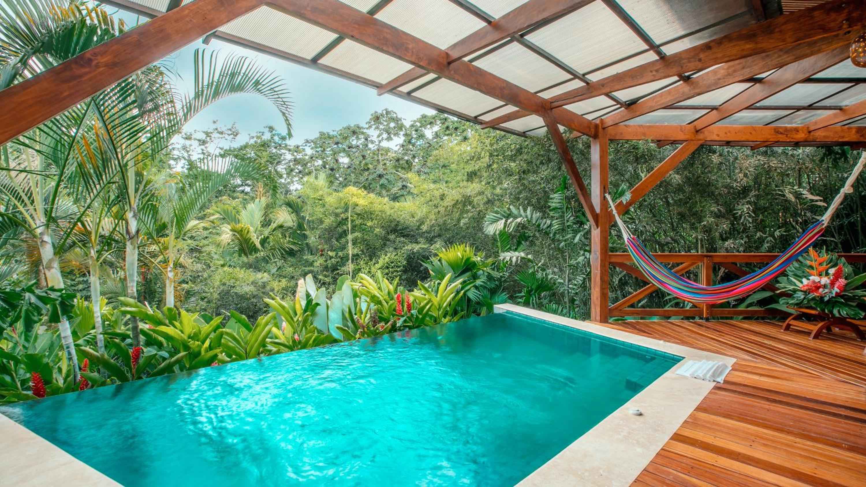 Infinity pool waters shimmer turquoise beneath a teak pergola, while tropical blooms frame this treetop sanctuary where hammocks sway above the rainforest canopy.