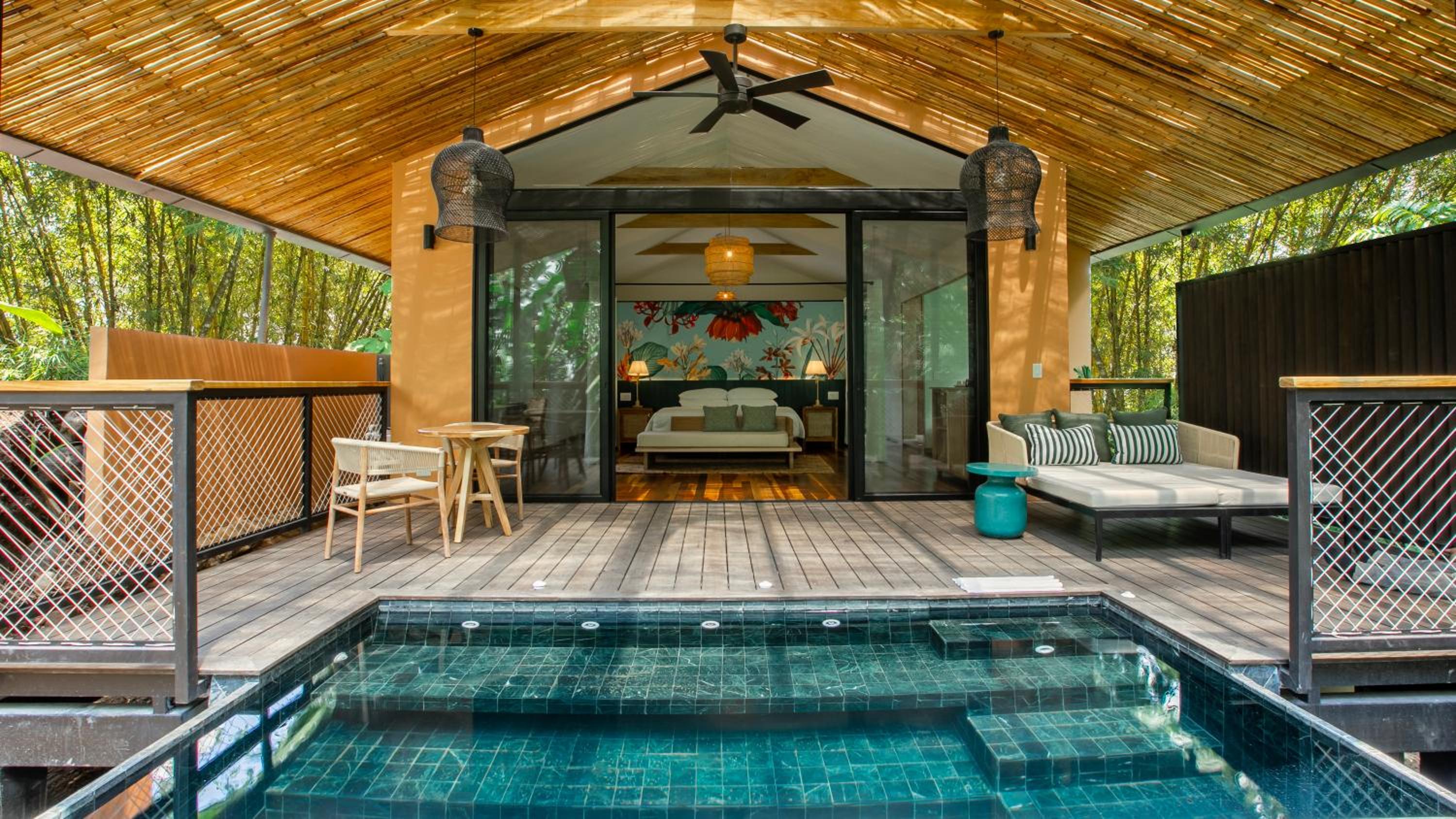 Bamboo-crowned suites open directly onto private plunge pools, where crystalline waters shimmer beneath filtered jungle light and woven pendant lamps cast golden shadows.