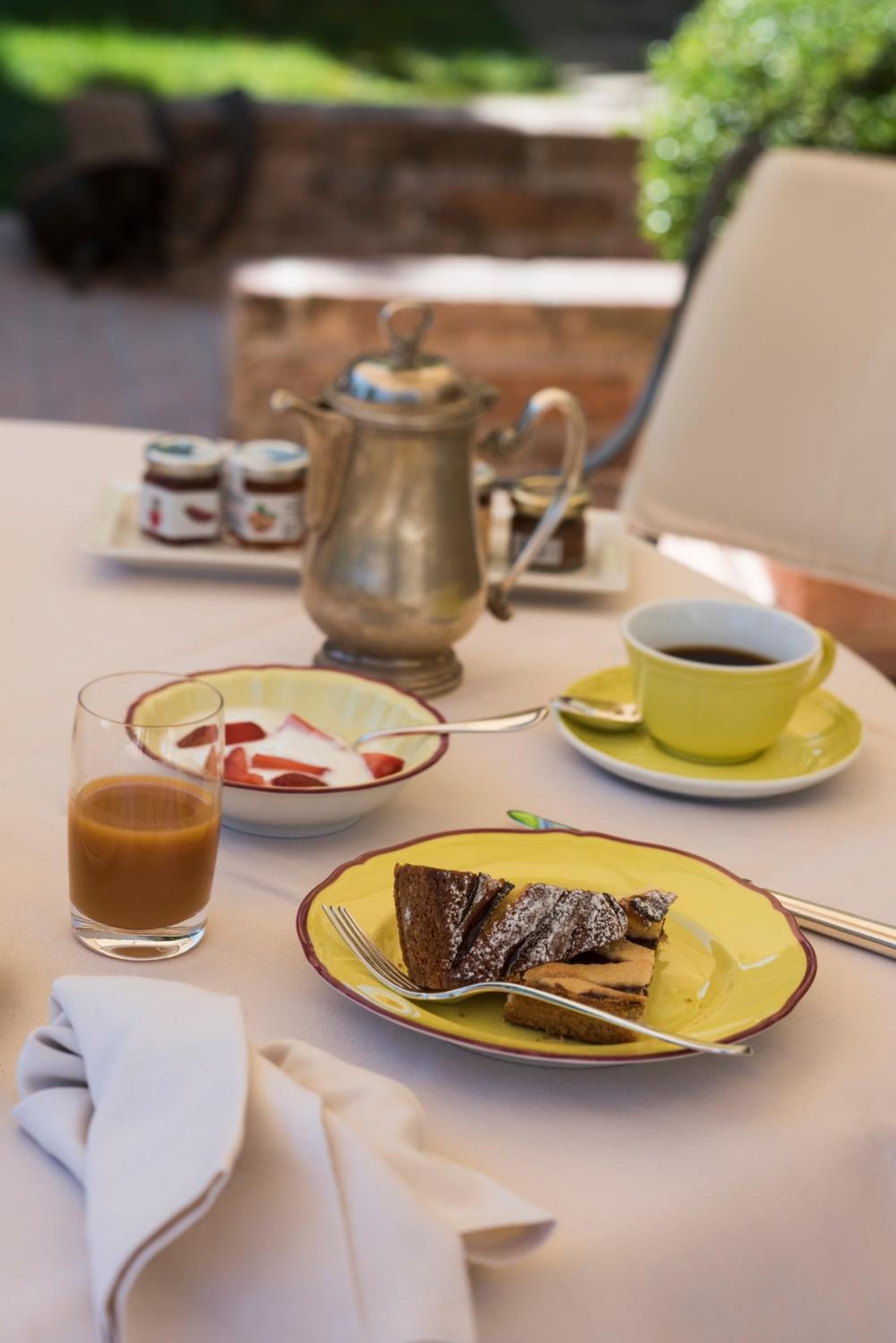 Morning light illuminates a refined breakfast spread featuring chocolate cake and rich espresso, served on hand-painted ceramics alongside vintage silver at this elegant Tuscan retreat.