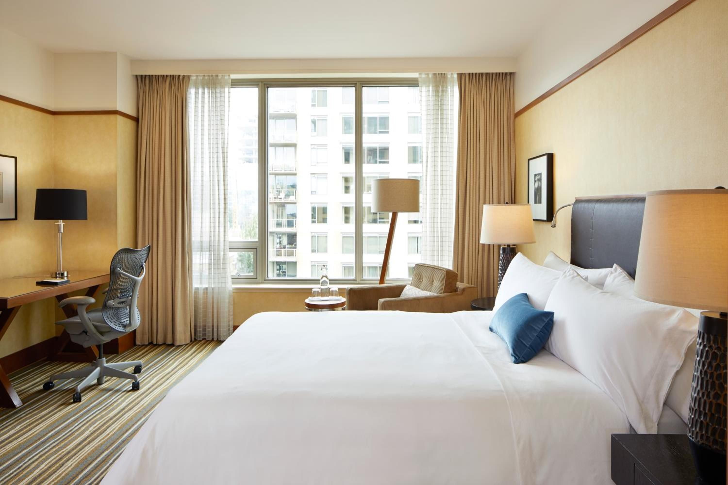 Floor-to-ceiling windows frame Seattle's urban landscape while warm wood accents and crisp white linens create a serene sanctuary above the bustling city streets.
