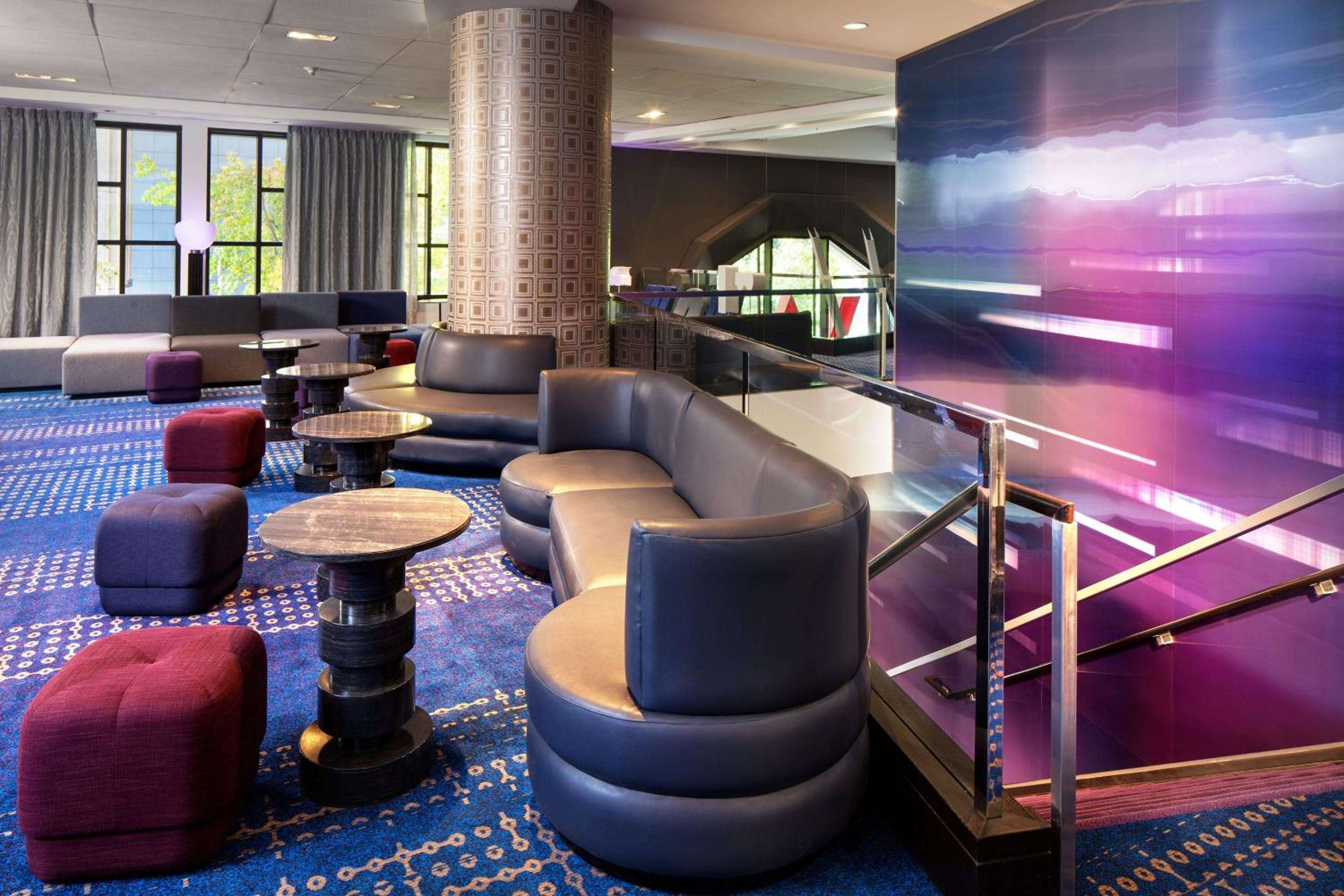 Dynamic purple digital art commands attention in this contemporary lobby where curved leather chairs and geometric blue carpeting create an energetic social hub.