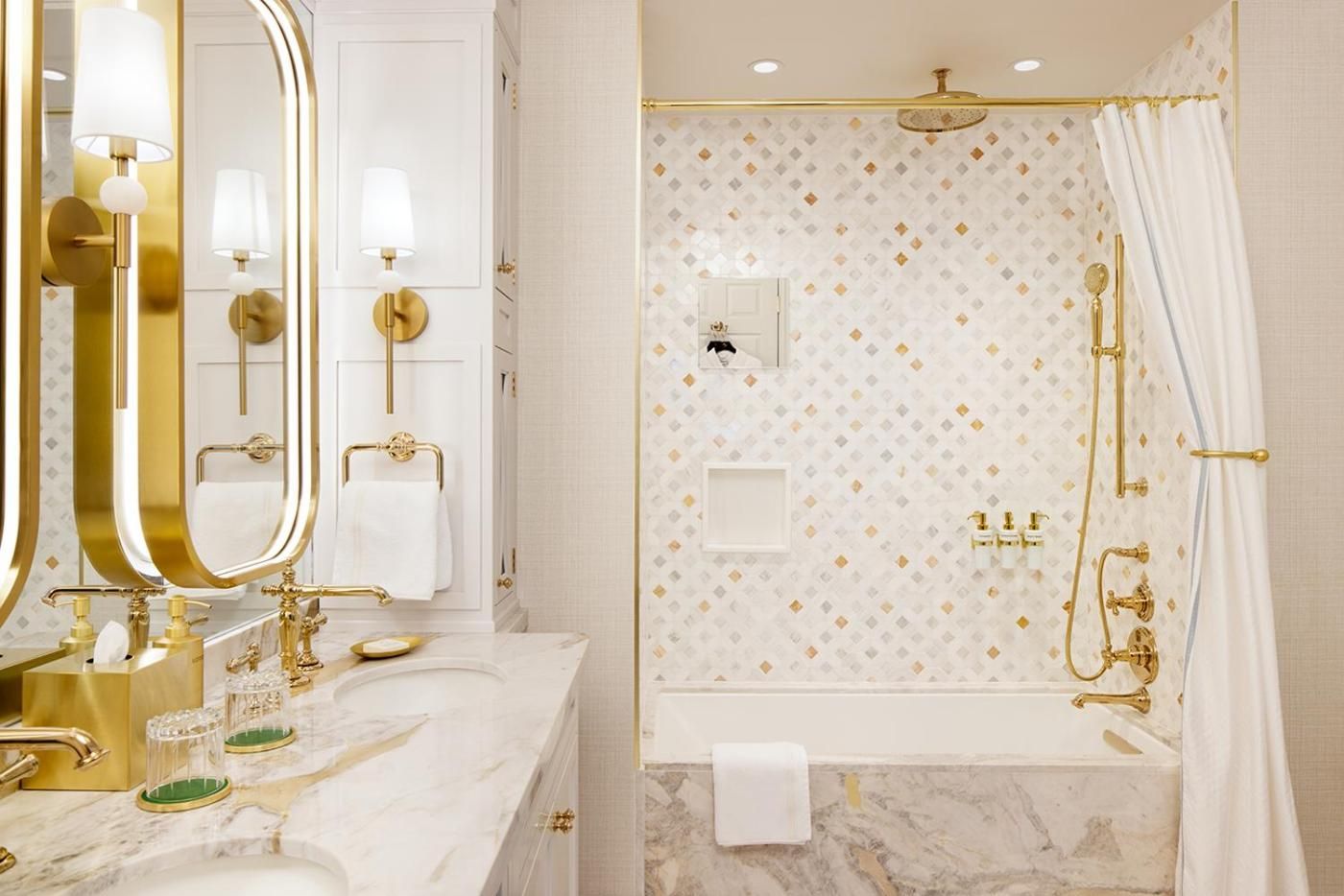 Gleaming brass fixtures and marble surfaces create an opulent retreat where geometric mosaic tiles catch morning light streaming through pristine white shutters.