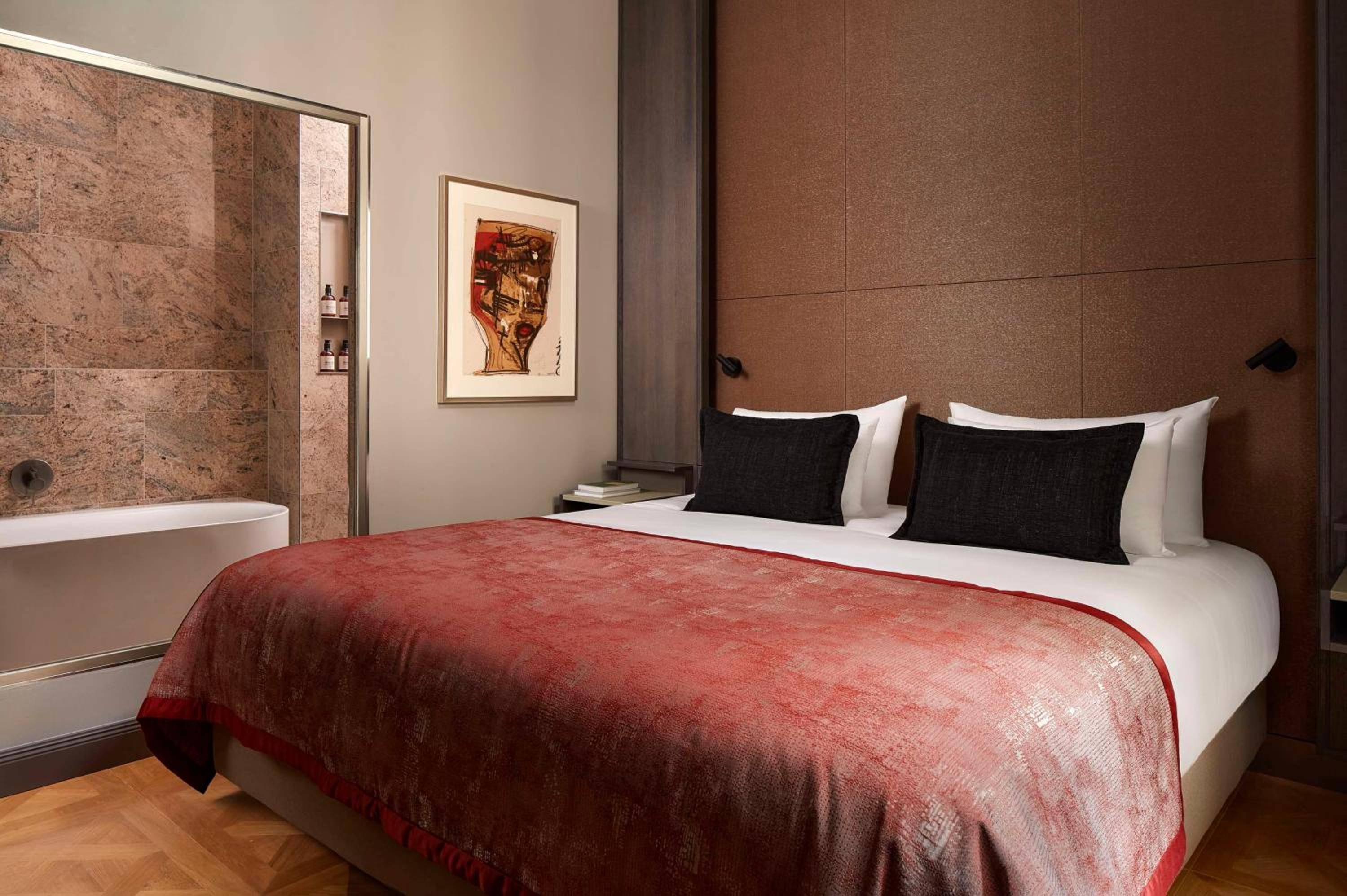 Warm timber headboards and burgundy velvet create intimate luxury, while marble-clad bathrooms glimpsed through glass doors add sophisticated drama to these thoughtfully designed suites.